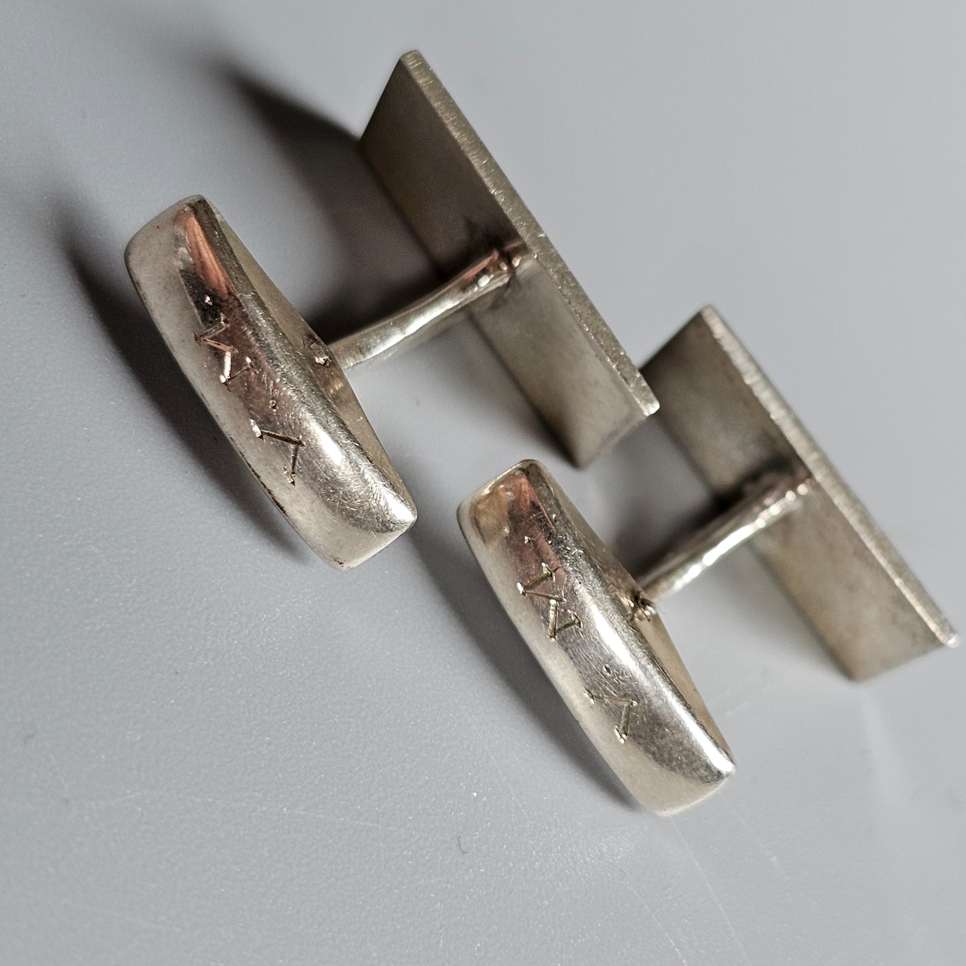 Pair of silver-toned metal cufflinks with engraved designs.