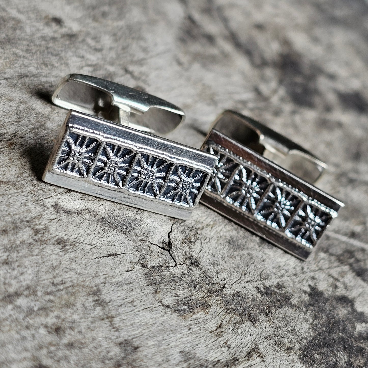 Silver cufflinks with an intricate floral or snowflake pattern engraved on their rectangular faces.