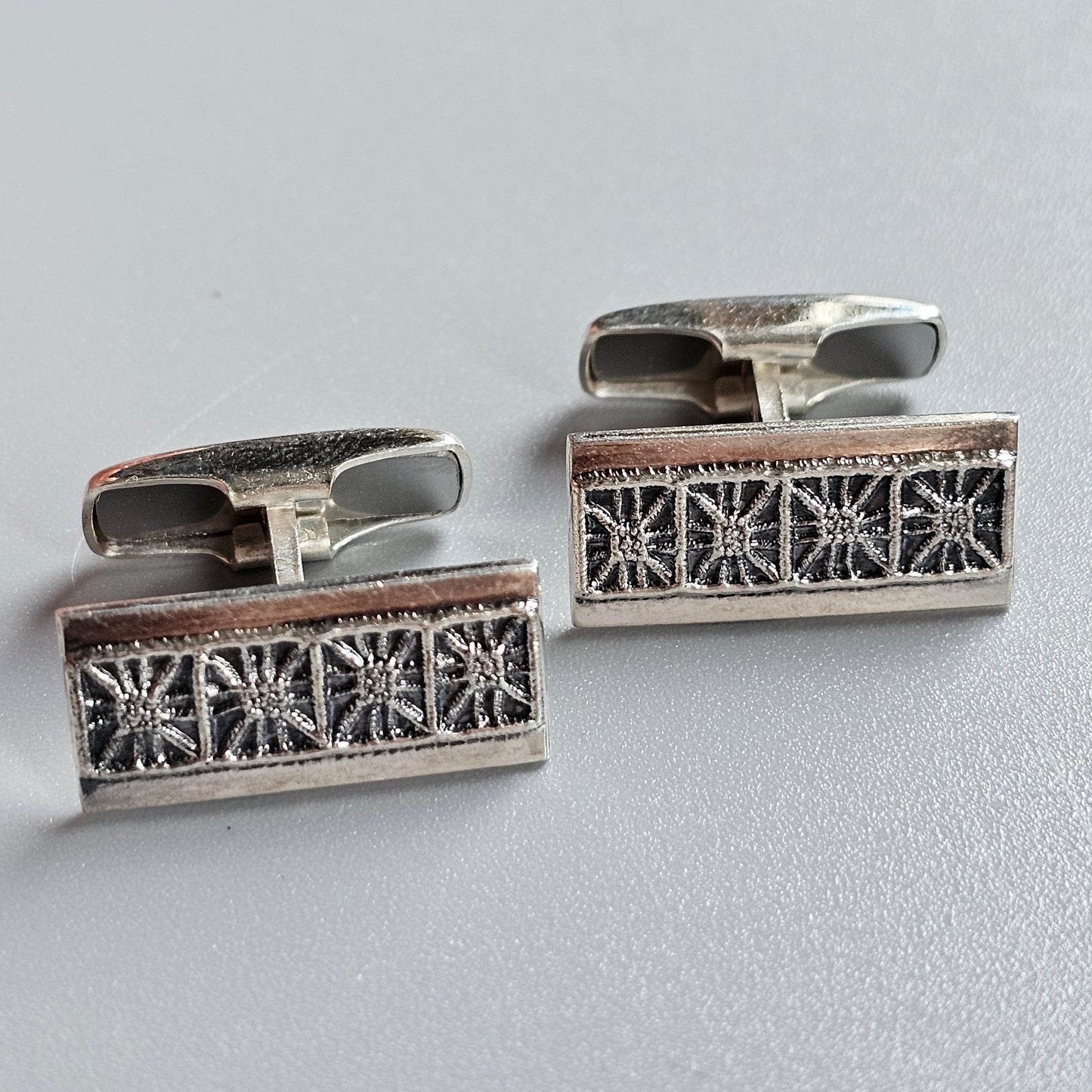 Pair of rectangular silver cufflinks with intricate snowflake-like patterns.