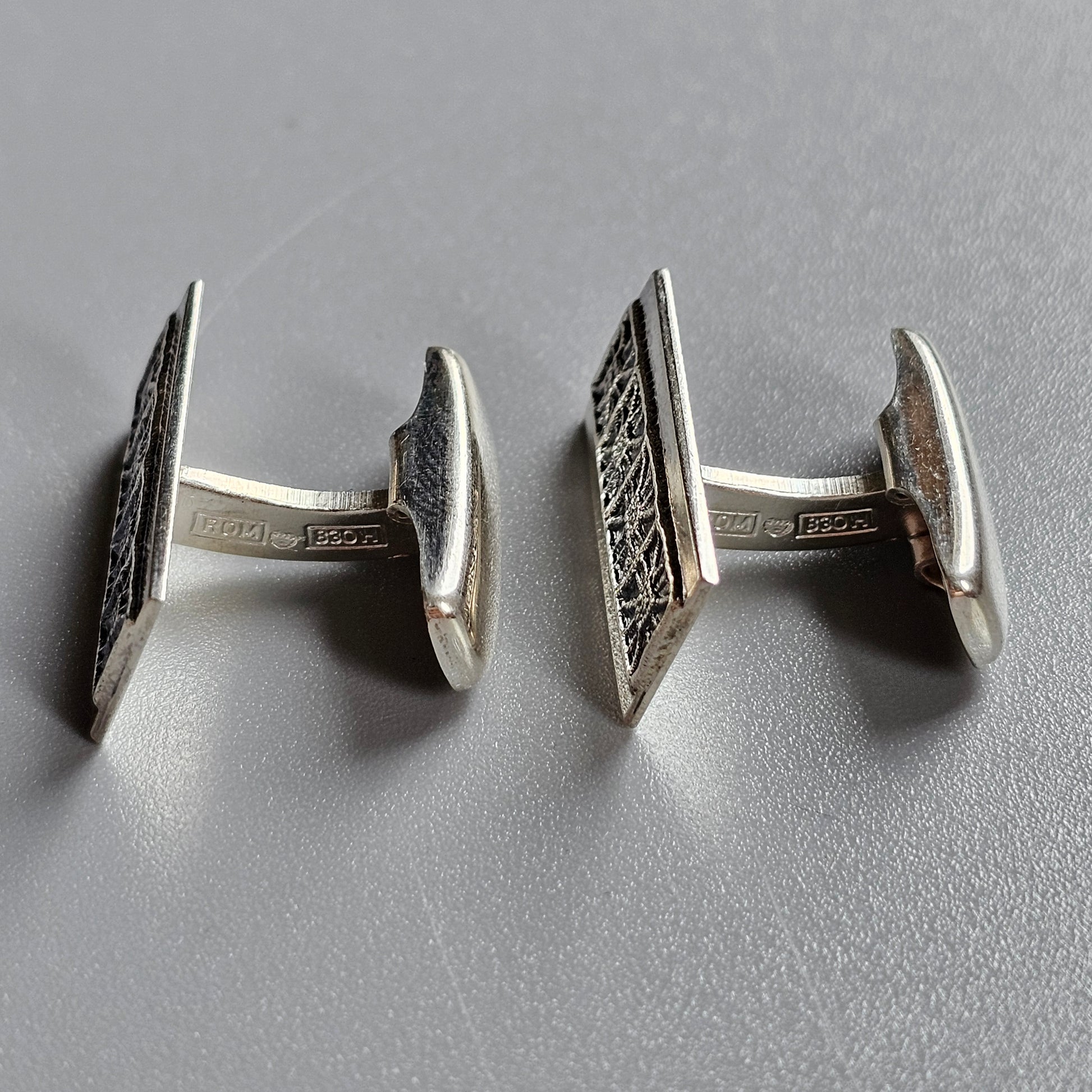 Pair of silver cufflinks with intricate geometric patterns on their faces.