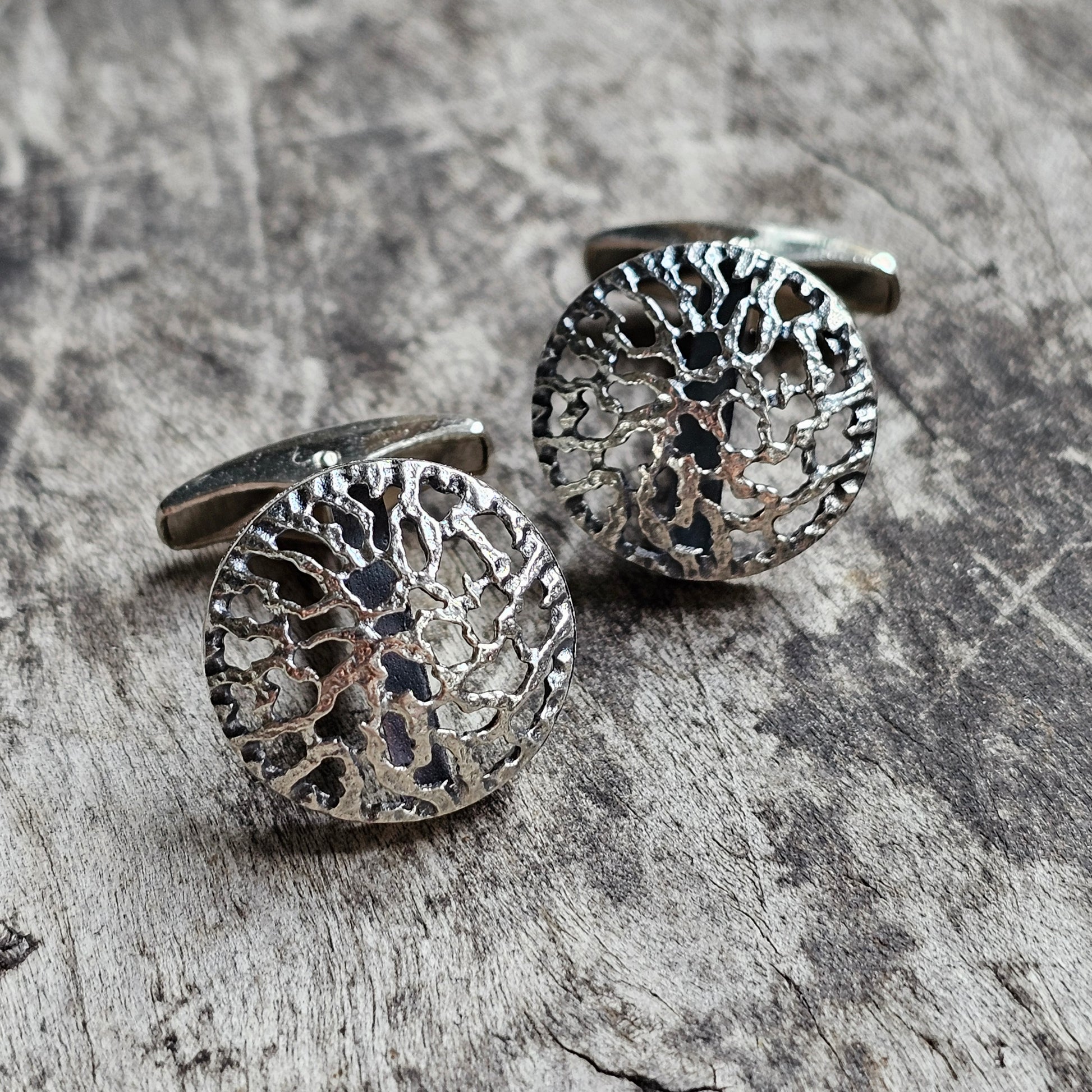 Pair of circular silver cufflinks with intricate filigree patterns.