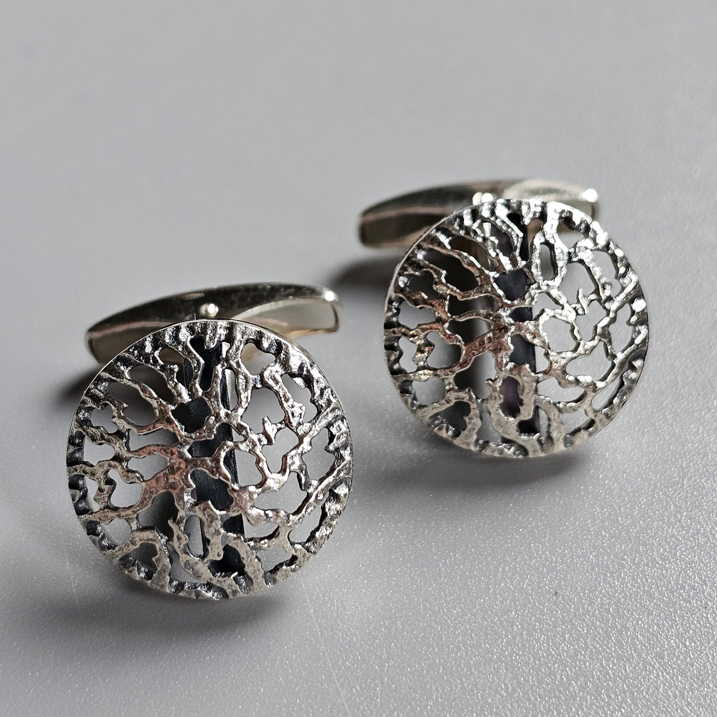 Pair of circular silver cufflinks with intricate tree-like designs.