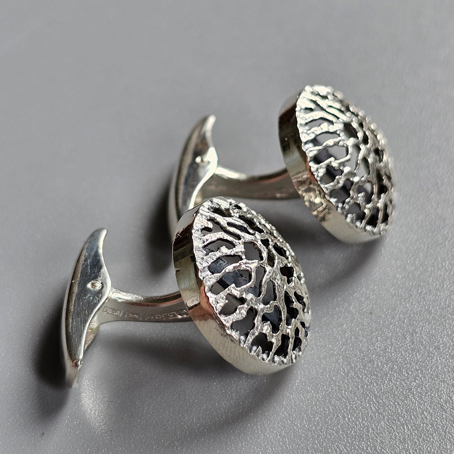 Pair of silver cufflinks with intricate filigree designs on circular faces.