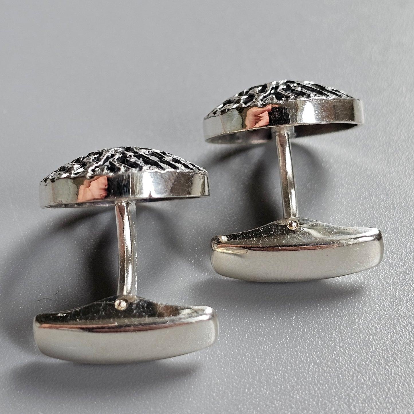 Pair of silver cufflinks with decorative floral patterns and copper accents.