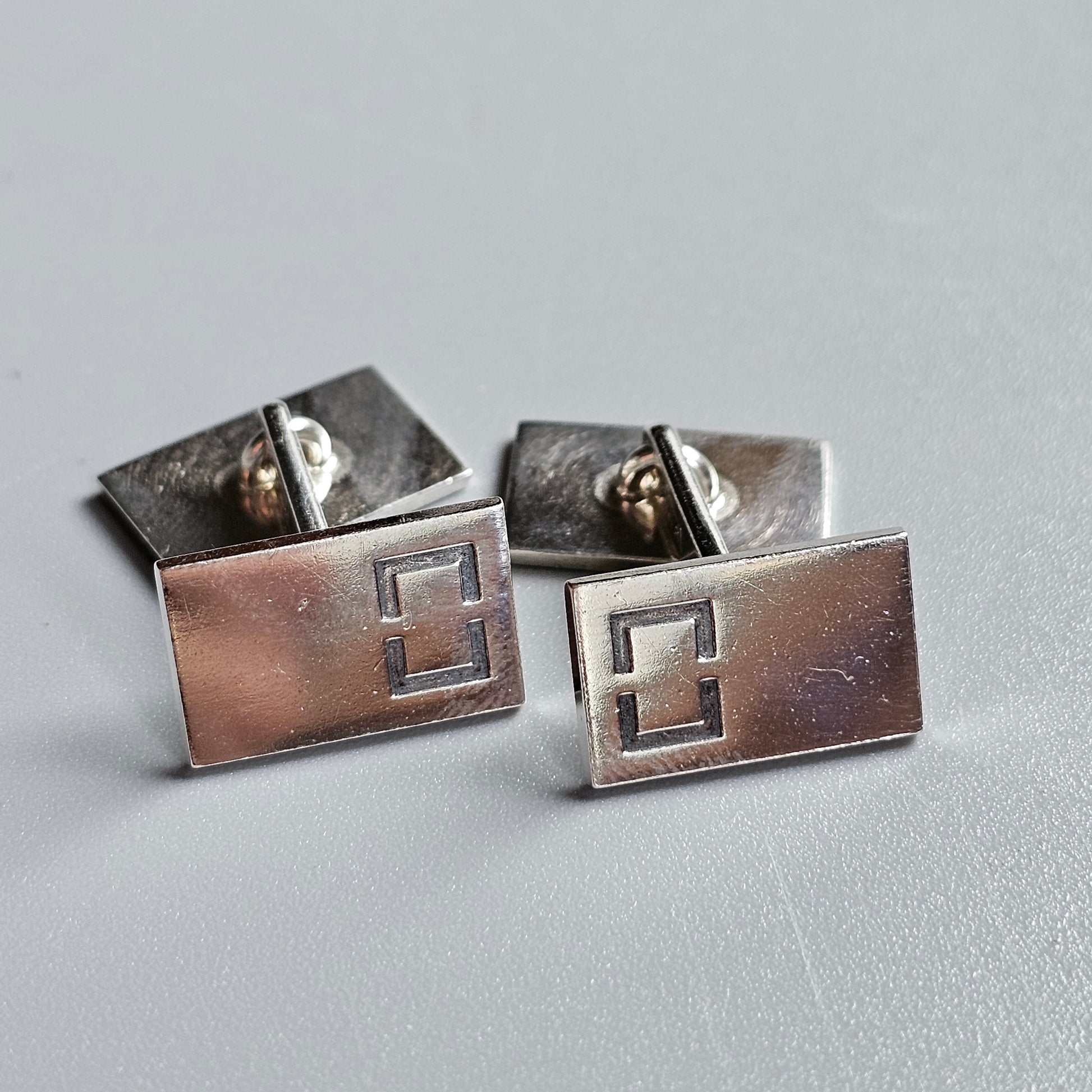 Pair of rectangular silver cufflinks with geometric cutout designs.