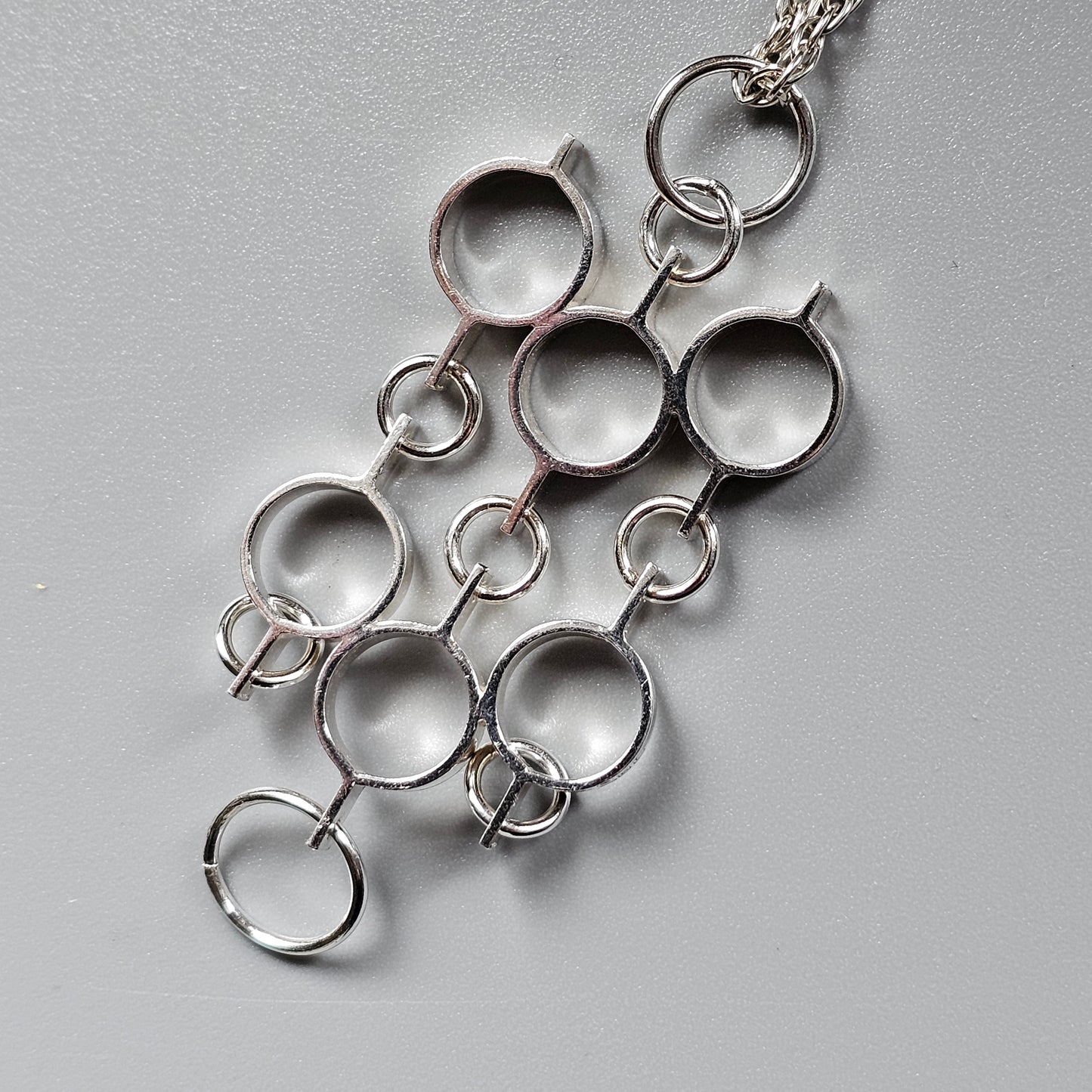 Silver pendant necklace with interconnected circular elements forming an abstract design.