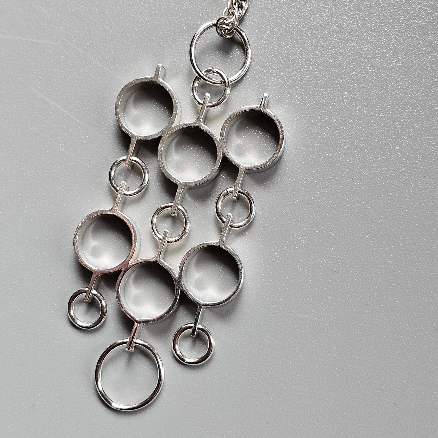 Silver pendant featuring interconnected circular shapes and rings in an abstract design.