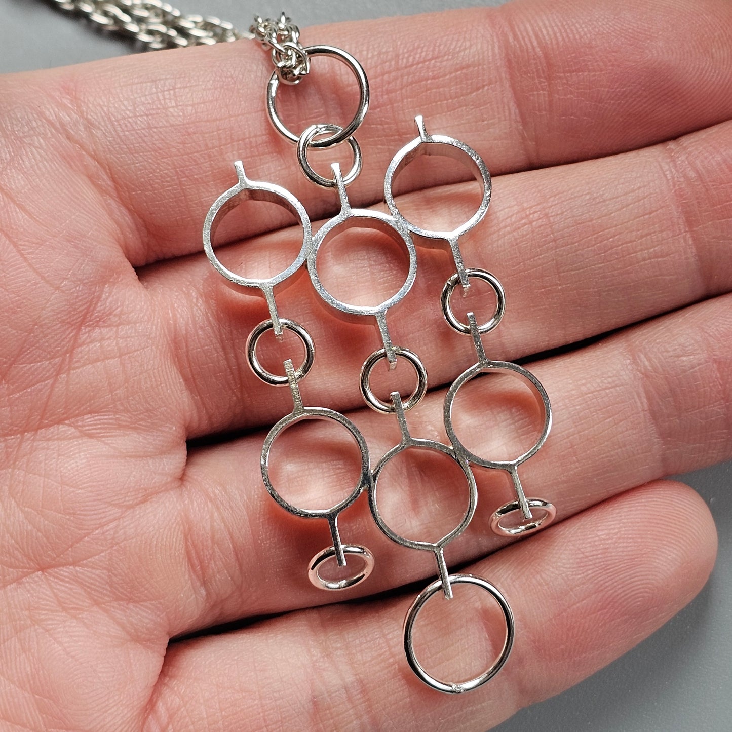 Silver pendant necklace with interconnected circular shapes.