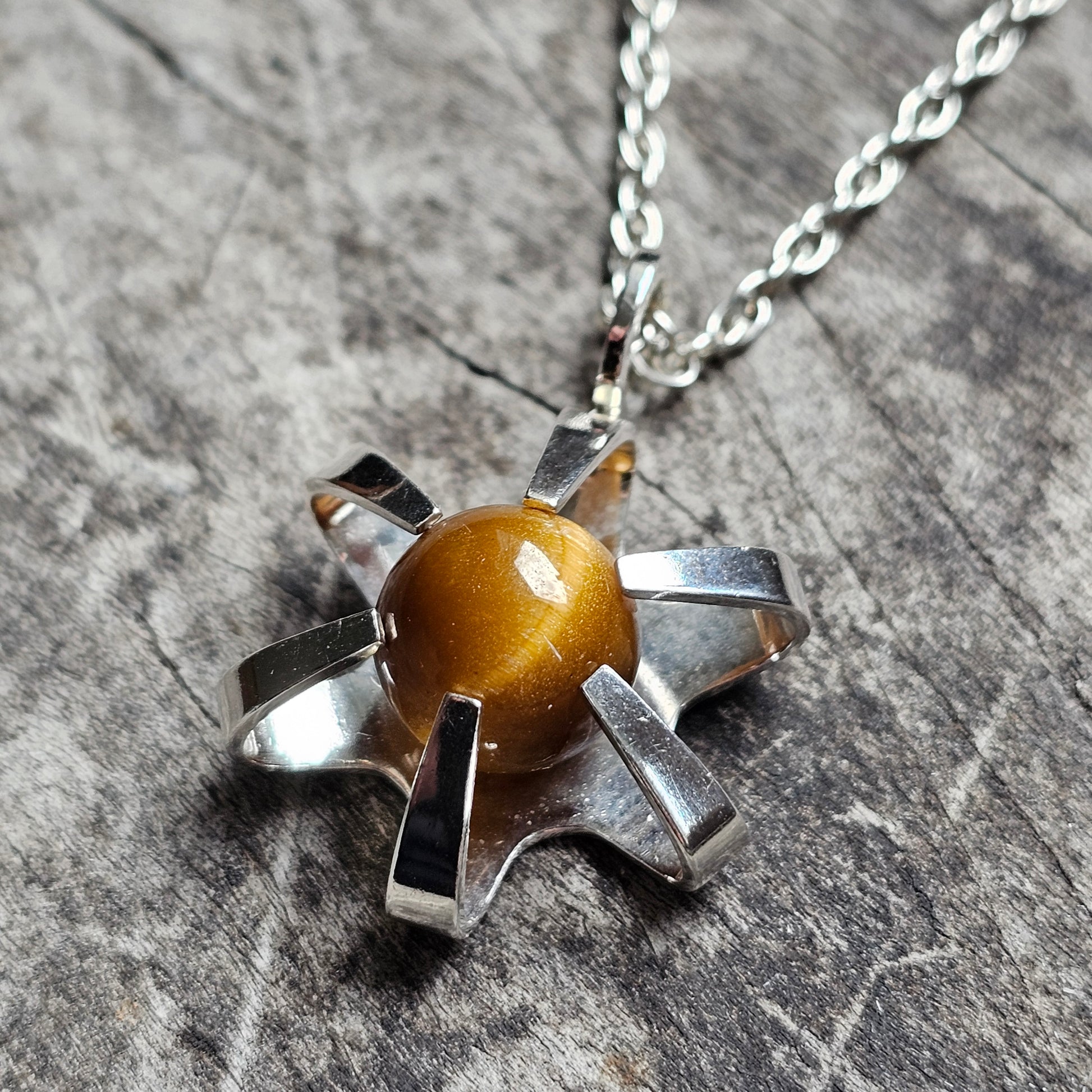 Silver star-shaped pendant with a round amber-colored stone in the center, hanging on a chain necklace.