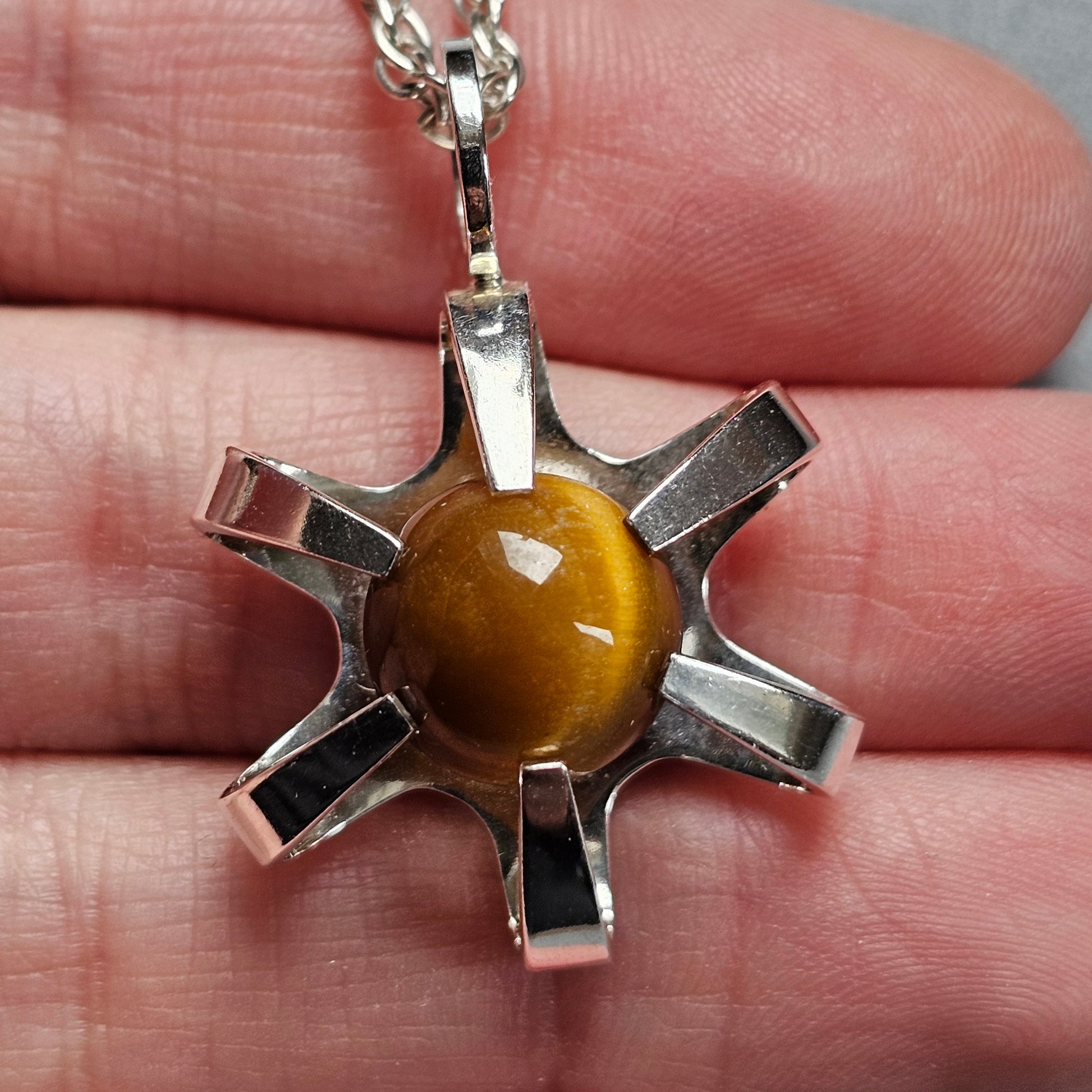 Silver star-shaped pendant with a round amber-colored stone in the center.