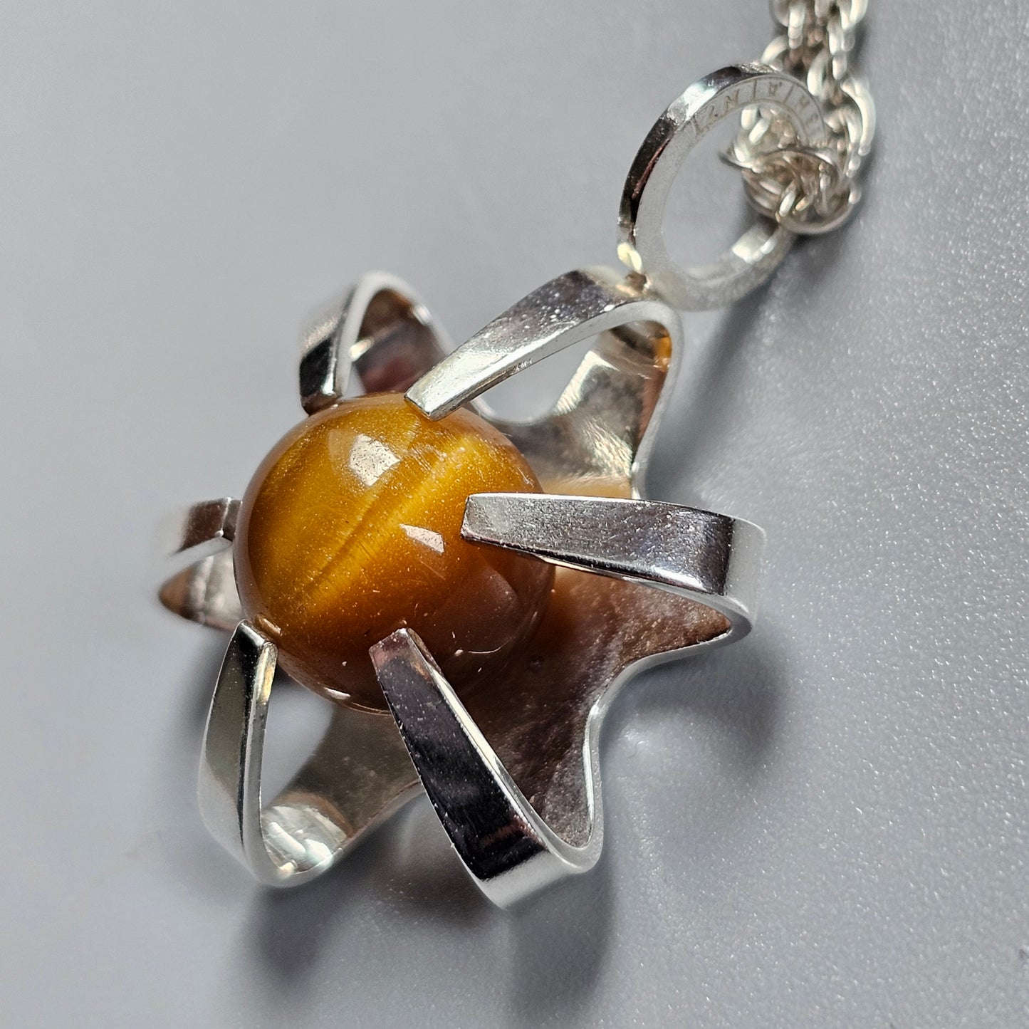 Silver star-shaped pendant with an amber-colored gemstone at its center.