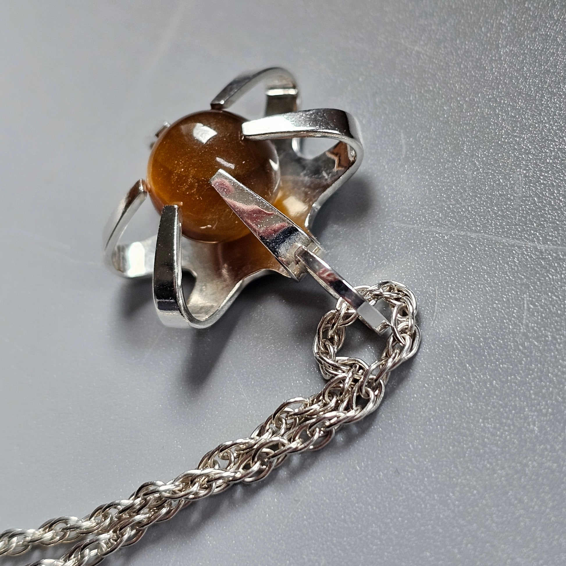 Silver pacifier pendant with an amber-colored nipple attached to a chain.