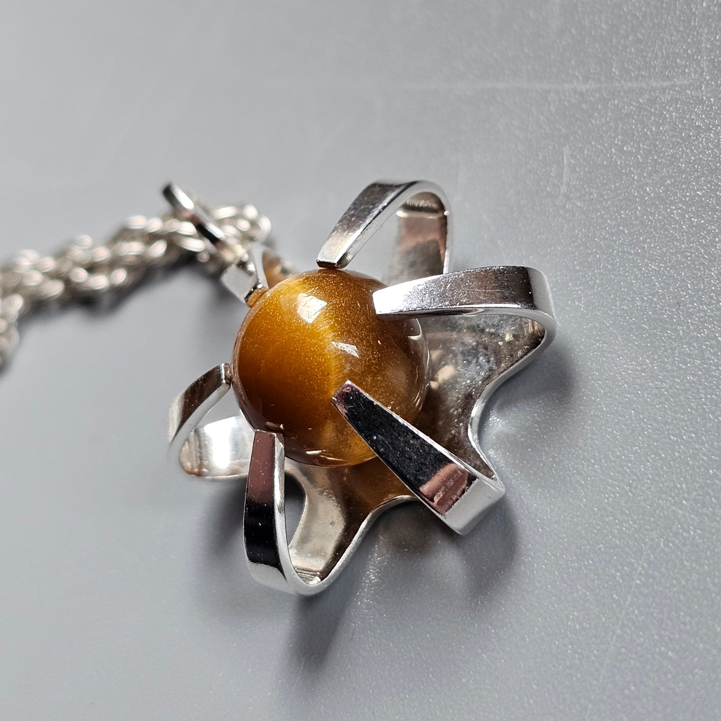 Silver pendant featuring a yellow-orange gemstone or bead held by petal-like metal prongs.