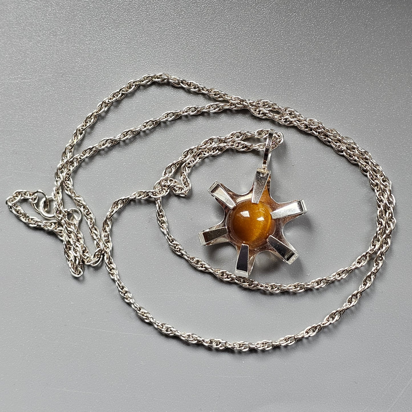 Silver pendant necklace featuring a sun-like design with an amber-colored center stone.