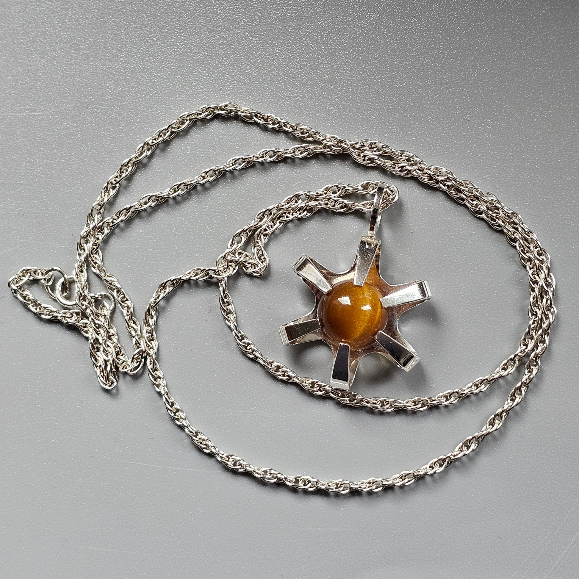 Silver pendant necklace featuring a sun-like design with an amber-colored center stone.