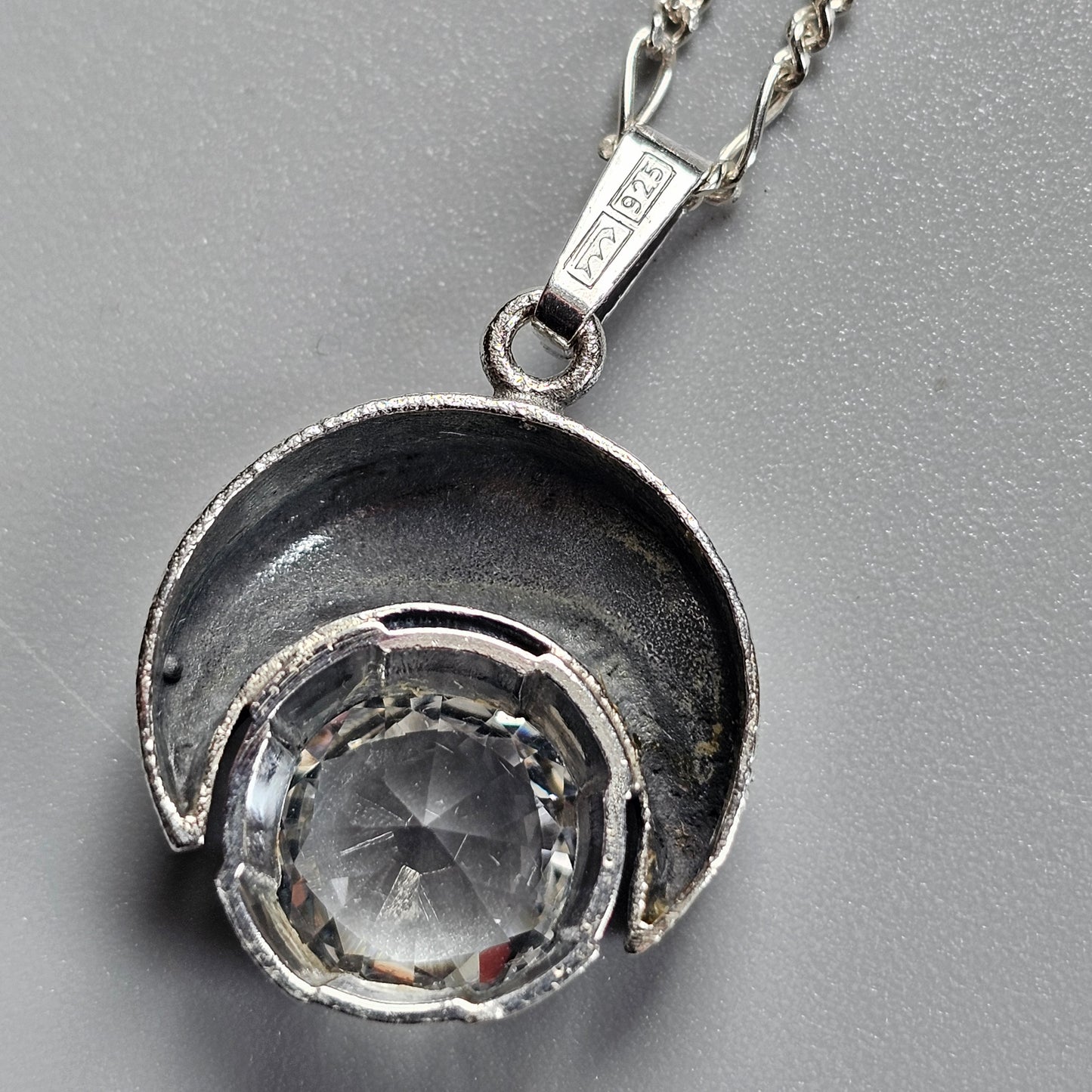 Silver pendant necklace featuring a crescent-shaped setting with a round crystal or gemstone.