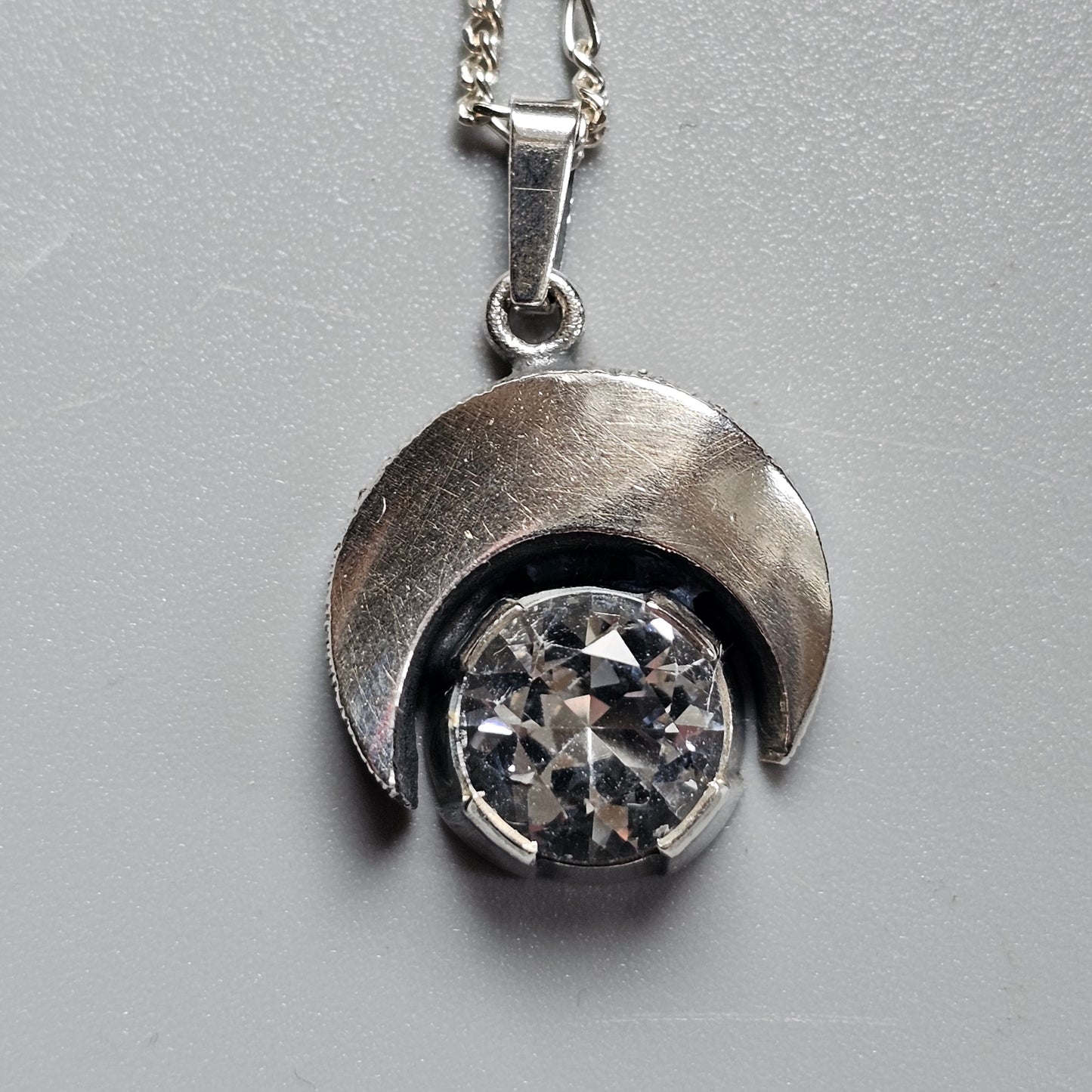 Silver pendant featuring a crescent shape cradling a round crystal or gemstone.