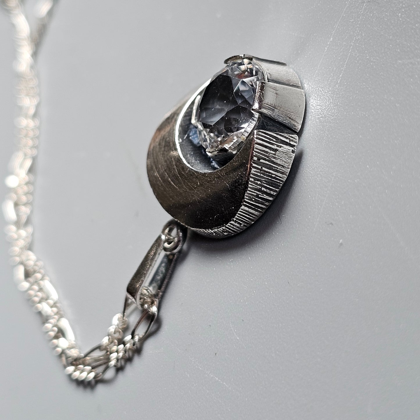 Metallic pendant necklace shaped like a broken egg with a tiny astronaut emerging from inside.