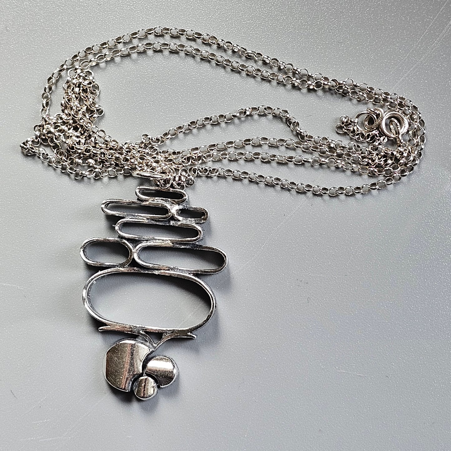 Abstract silver pendant necklace with interconnected oval shapes and small spheres.