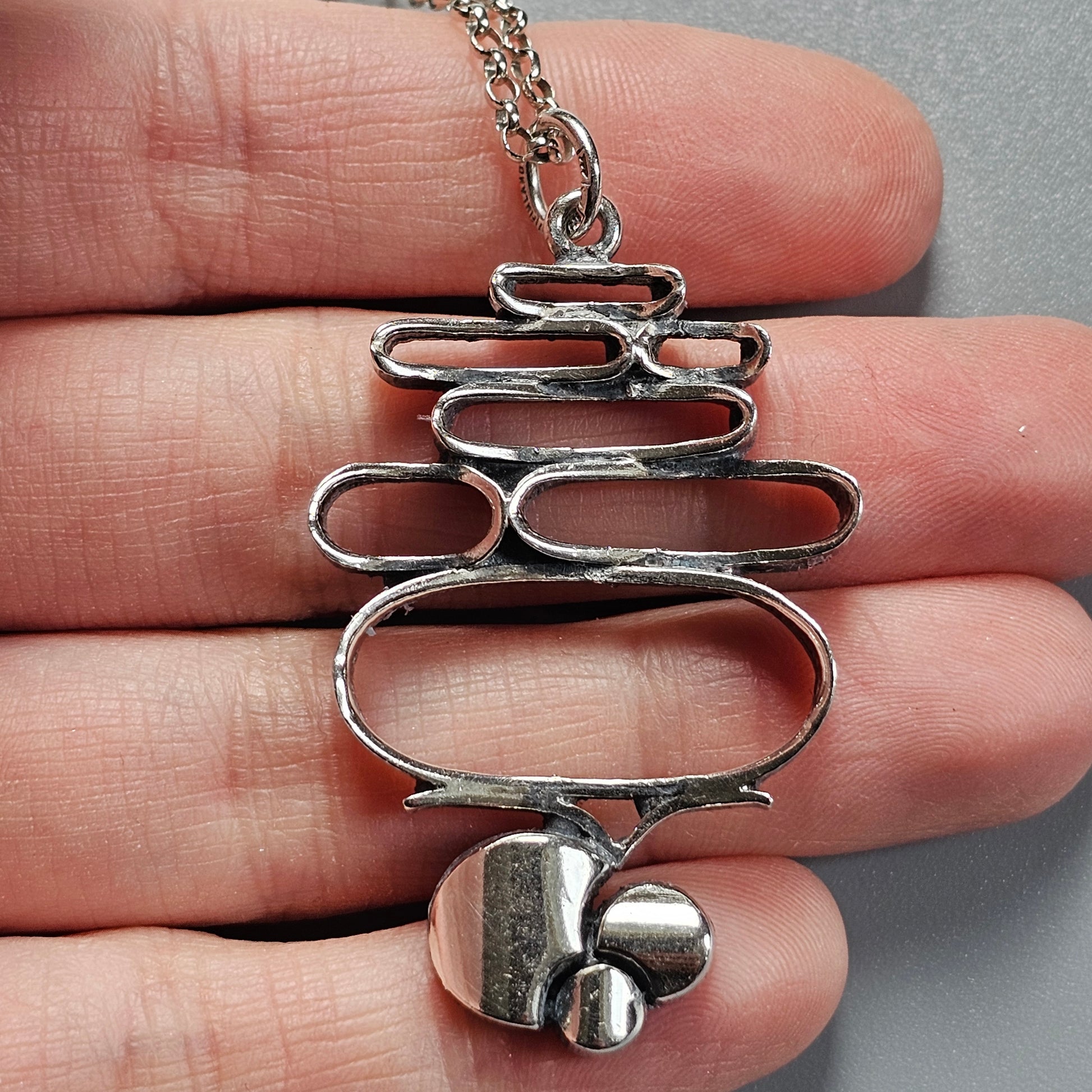 Silver pendant necklace with an abstract, stacked oval design and small spherical elements at the bottom.