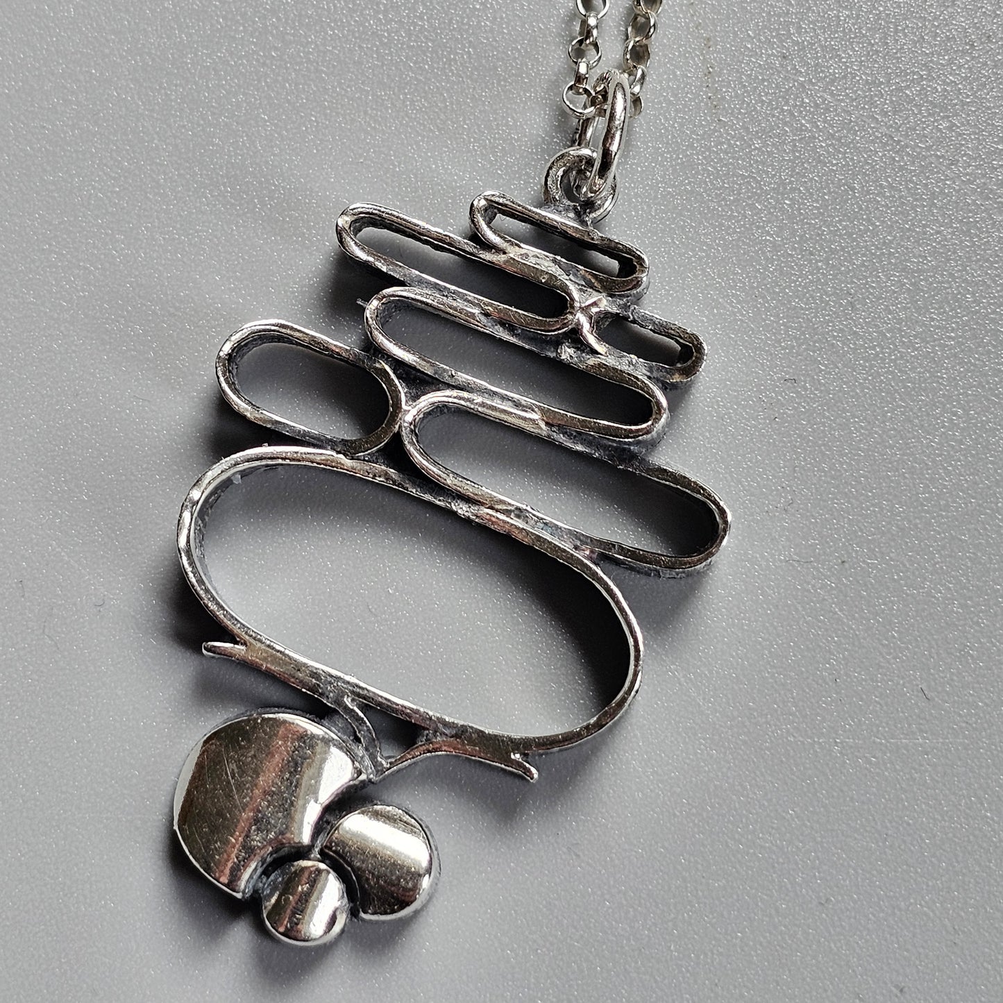 Silver pendant necklace with a wavy, ribbon-like design and small spherical elements at the bottom.