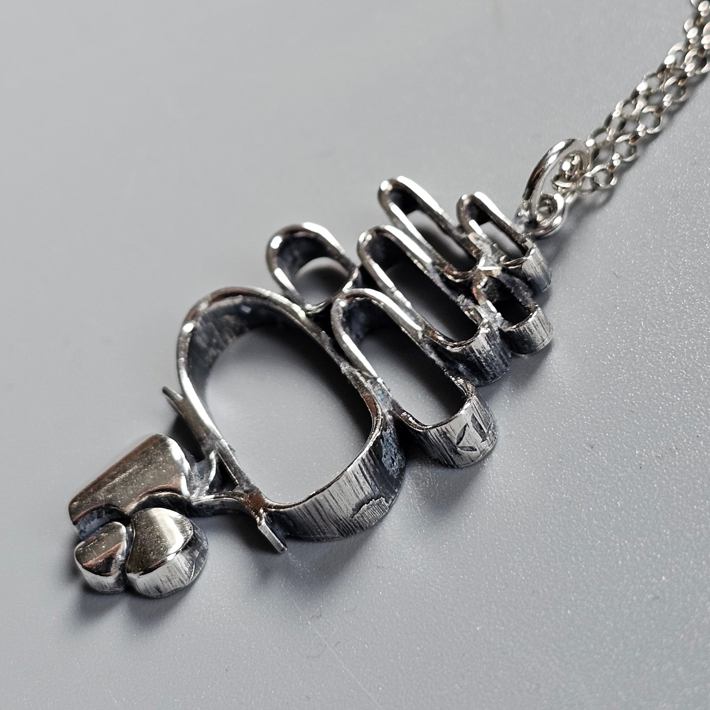 Silver pendant necklace shaped like the word ’Ouch’ with a small skull charm attached.