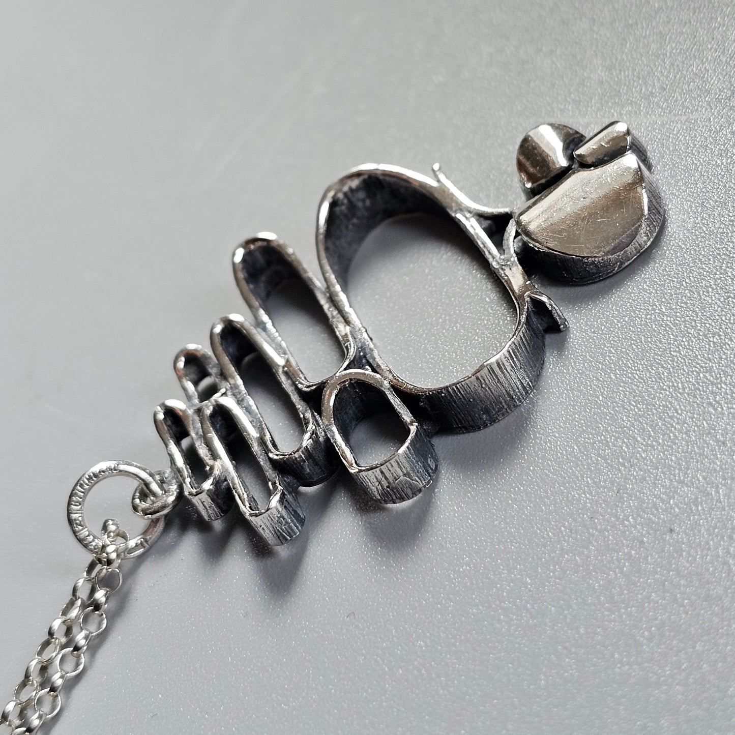 Silver-toned metal pendant shaped like brass knuckles with a chain attached.