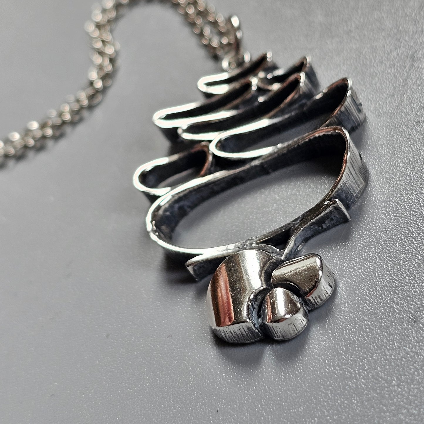 Silver pendant necklace shaped like an abstract wave or flame design.