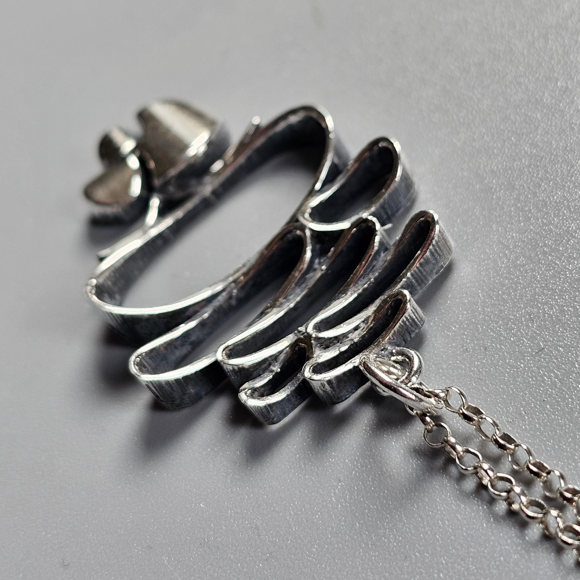 Silver pendant shaped like an abstract wing or feather, attached to a delicate chain.