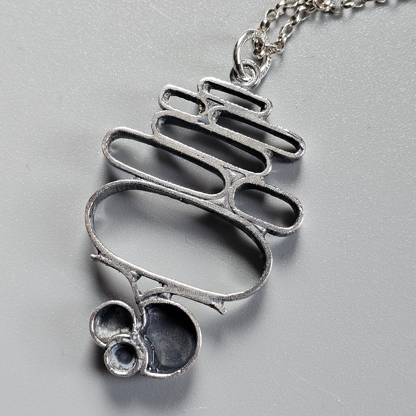 Silver pendant necklace with an abstract, curvy design resembling a stylized skeleton or ribcage.