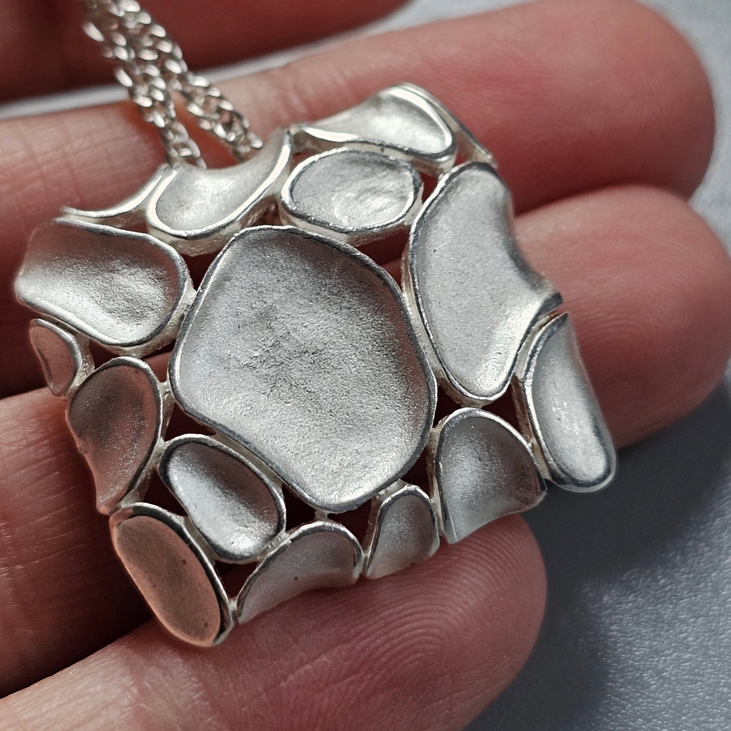 Silver pendant necklace with an organic, pebble-like design.