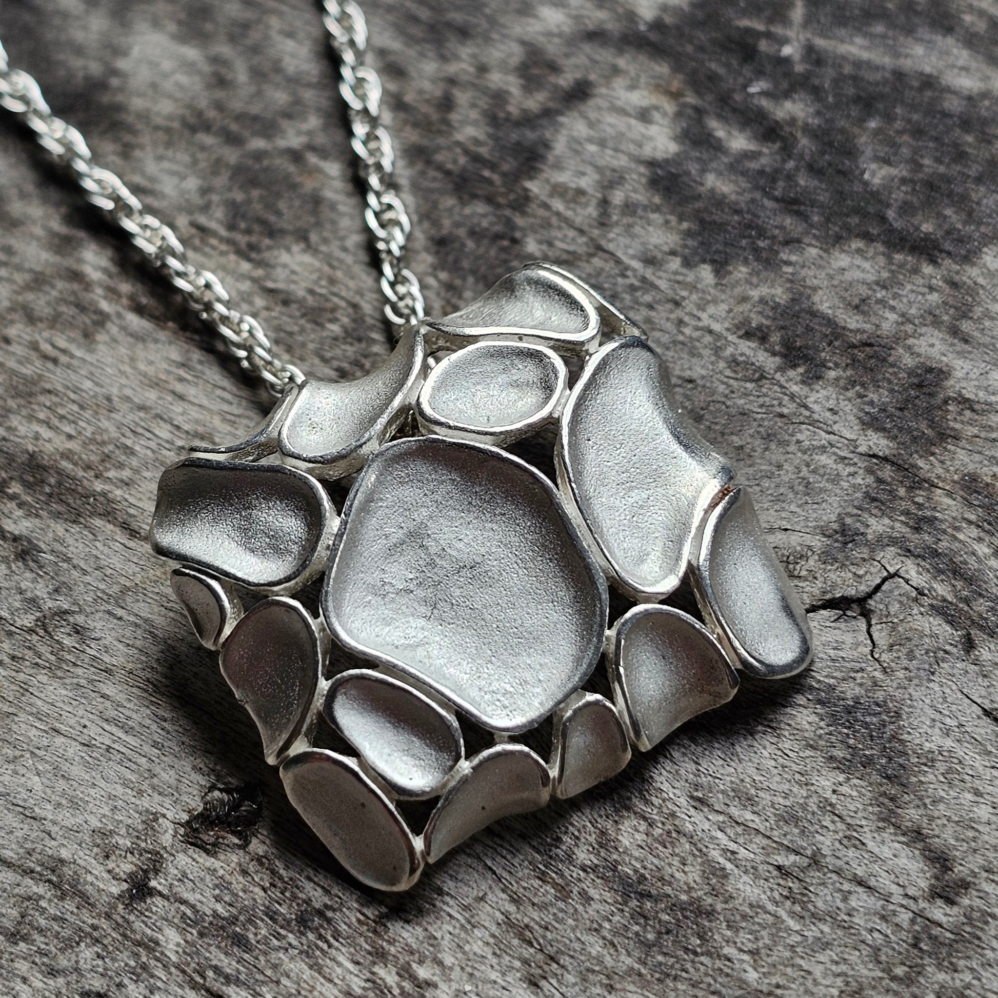 Silver pendant with an organic, pebble-like design on a chain necklace.