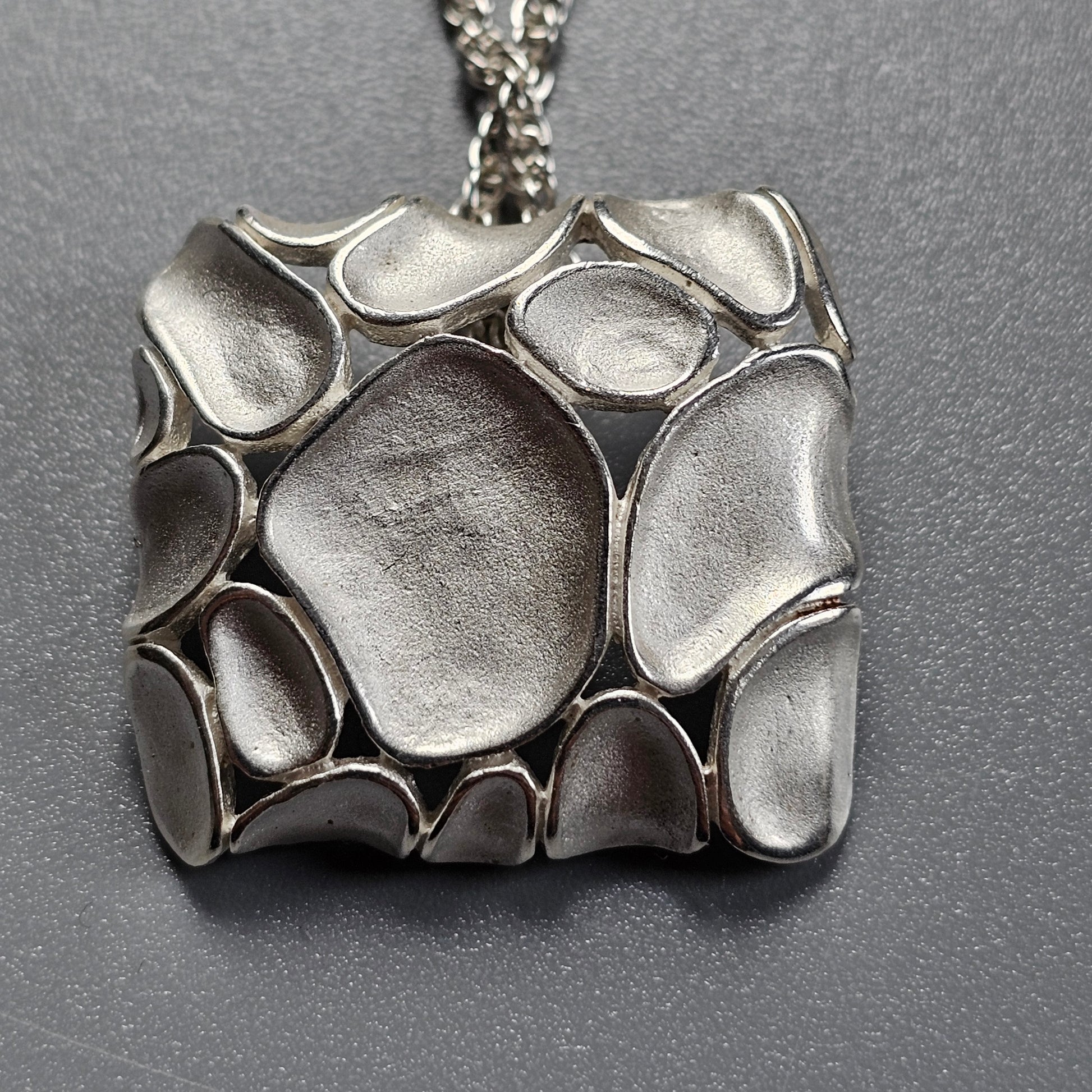 Silver pendant with an organic, pebble-like pattern.