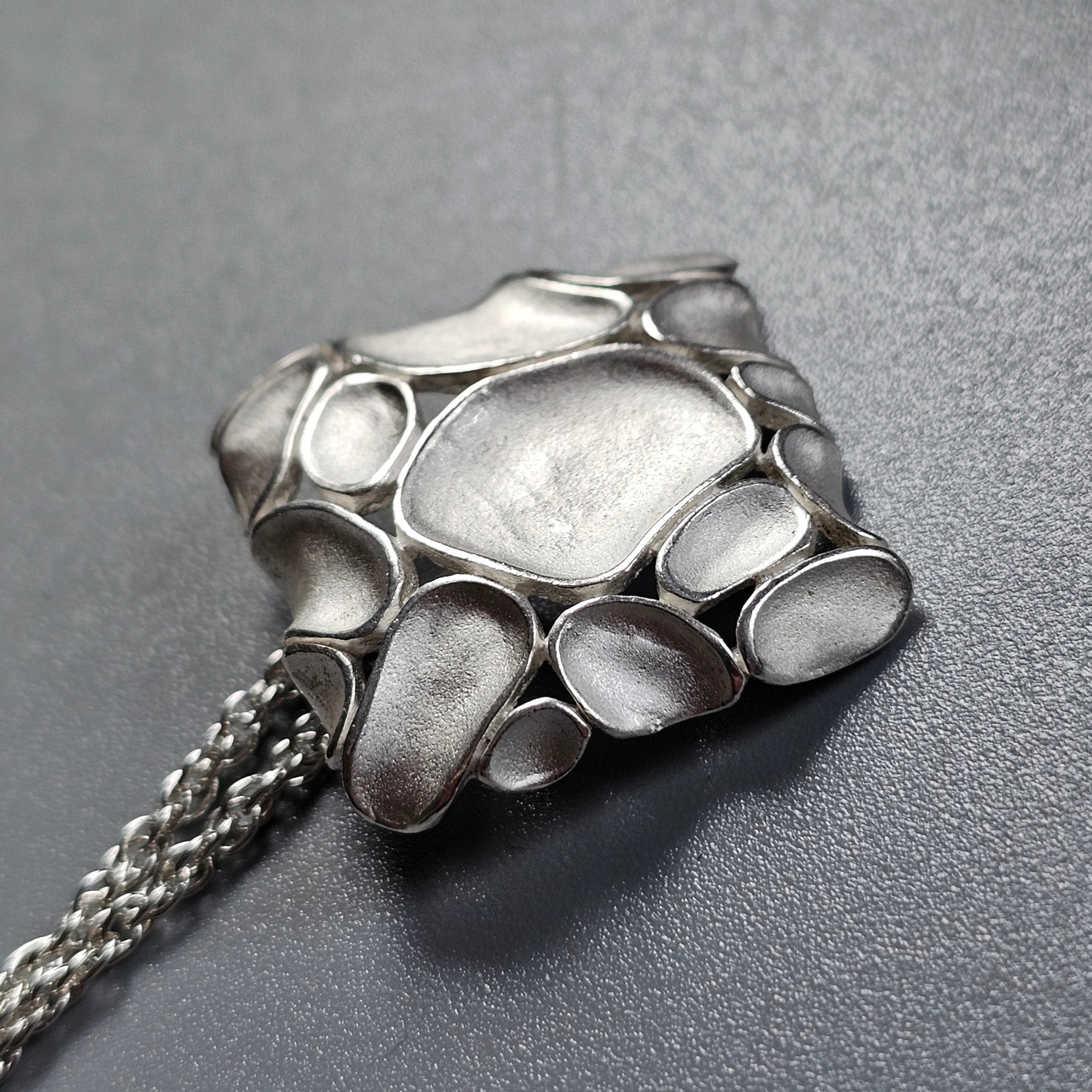 Silver pendant shaped like a stylized animal paw or claw on a chain.