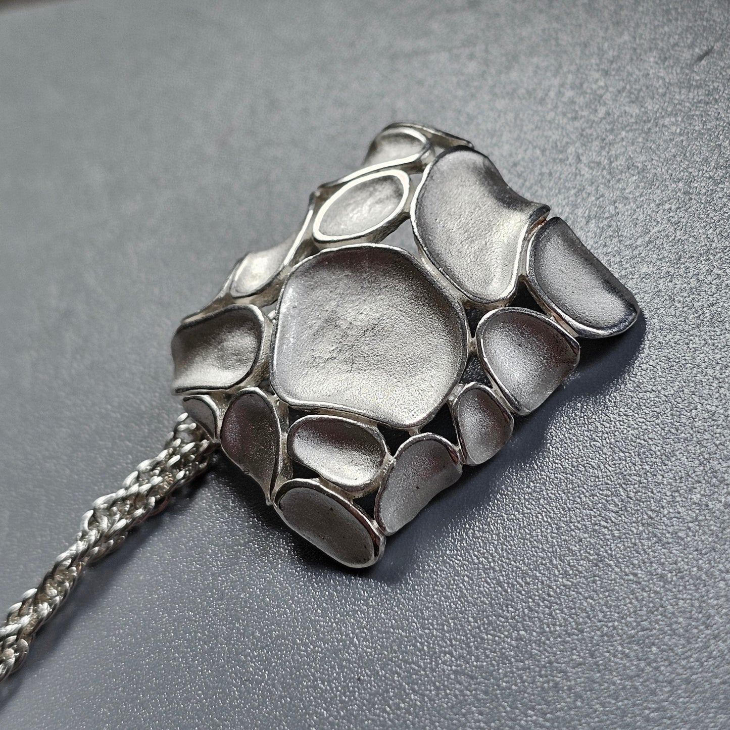 Silver pendant with an organic, pebble-like design on a chain.