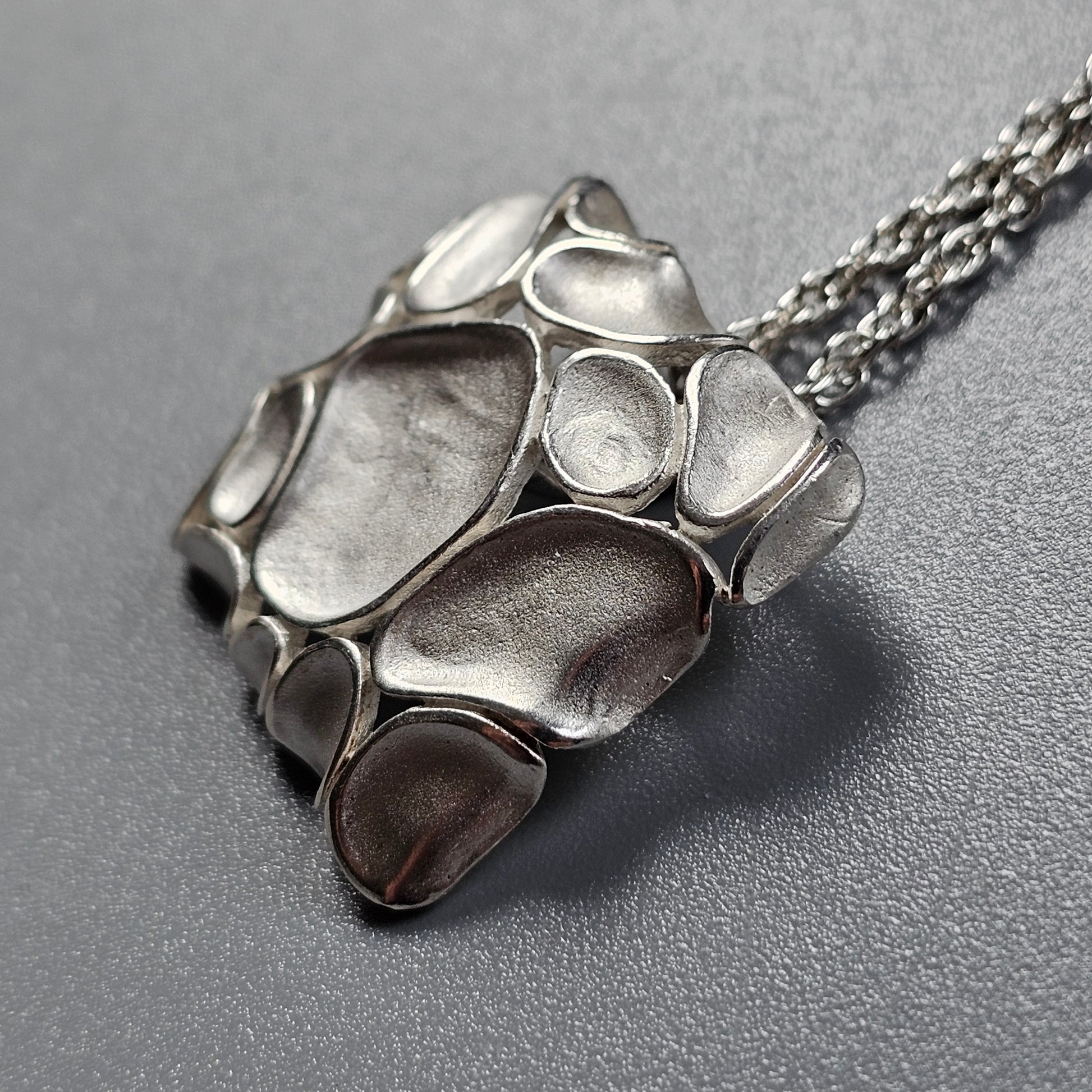 Silver pendant with an organic, pebble-like design on a chain necklace.