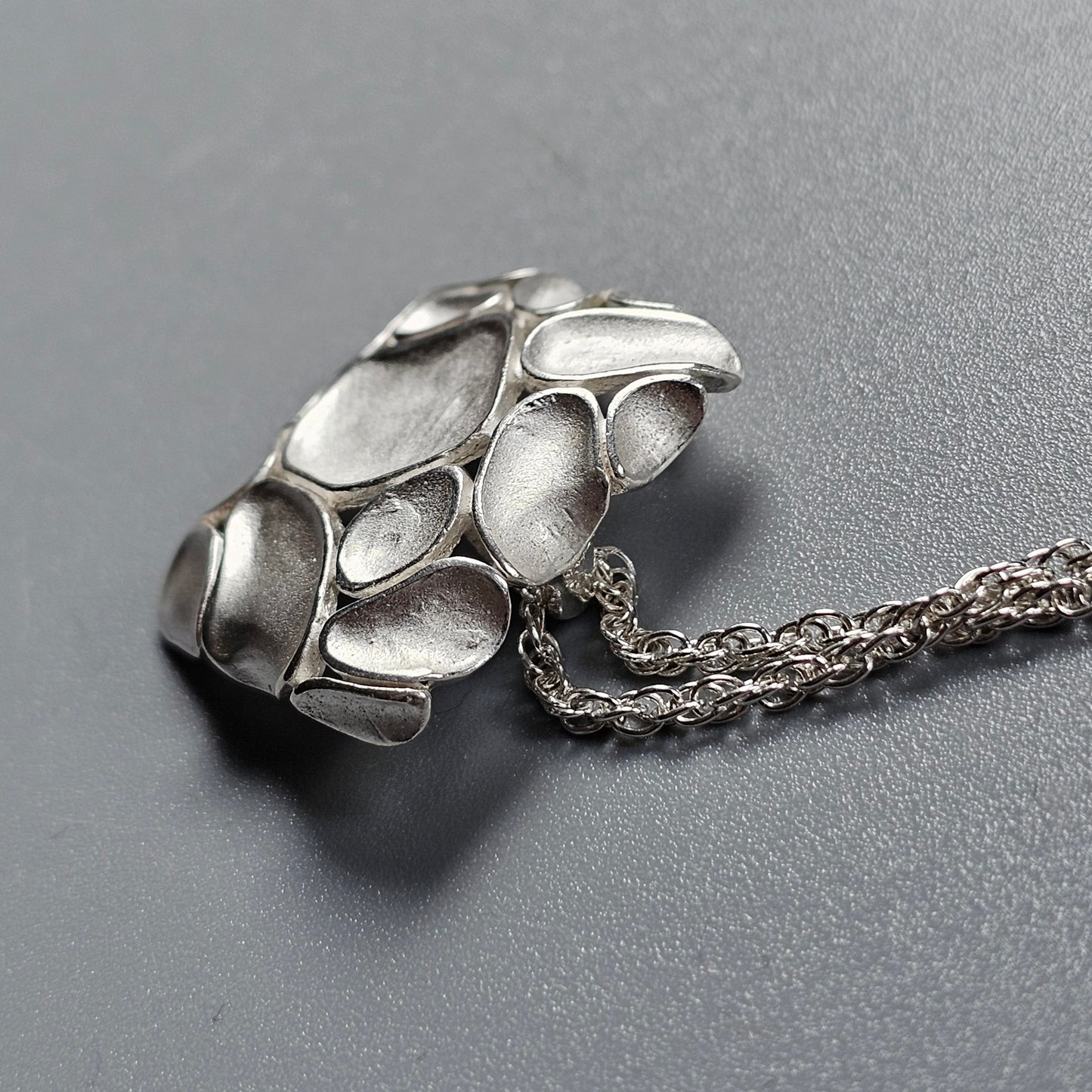 Silver pendant with an organic, pebble-like design attached to a chain.