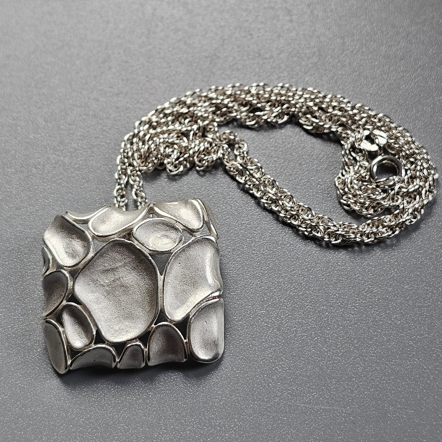 Silver pendant with an organic, pebble-like design attached to a chain necklace.