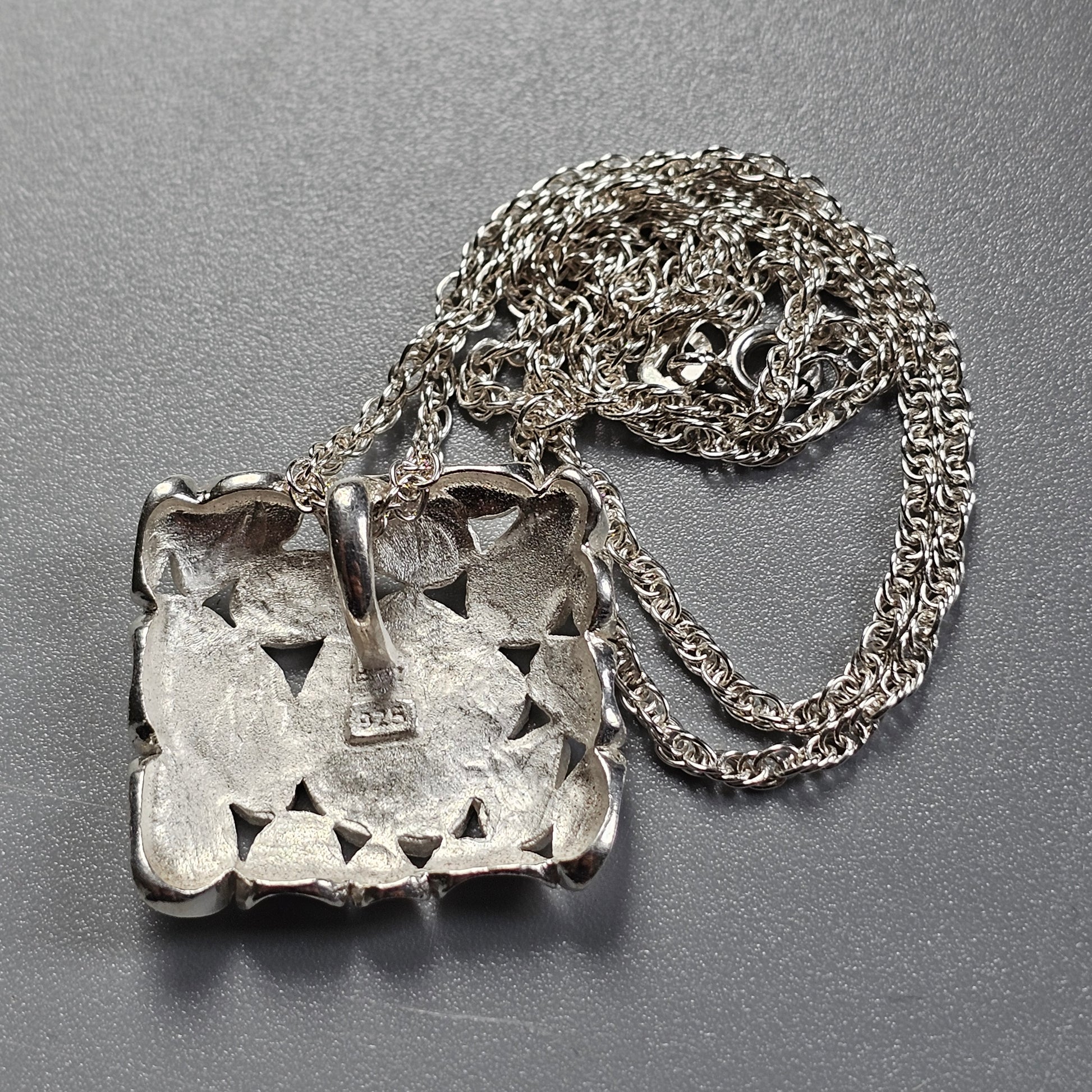 Silver pendant with a geometric cutout pattern attached to a chain necklace.