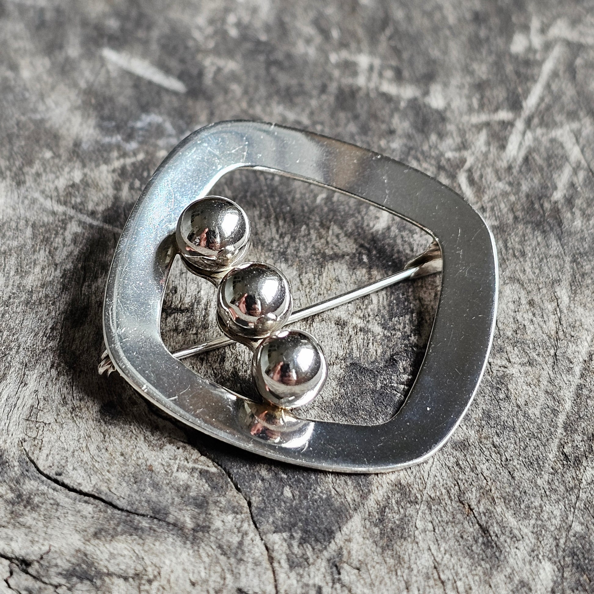 Silver brooch or pin with an abstract oval shape and three metallic spheres.