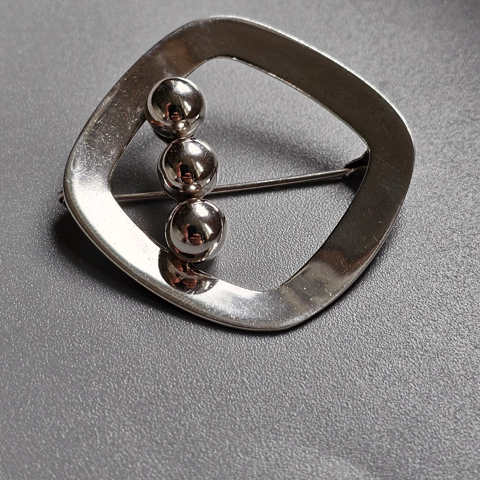 Silver belt buckle with three spherical studs arranged vertically.