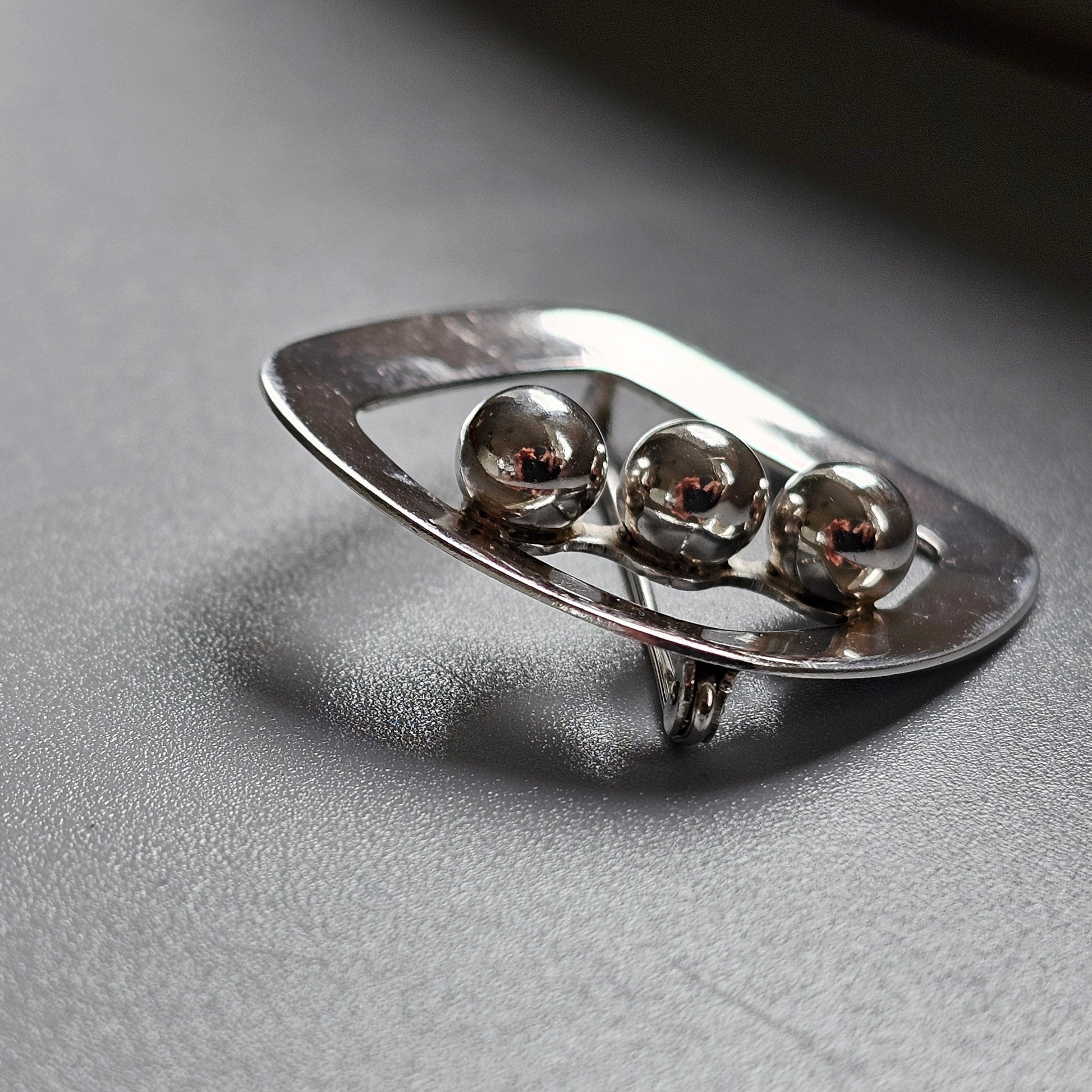 Oval silver brooch or pin featuring three metallic spheres arranged in a row.