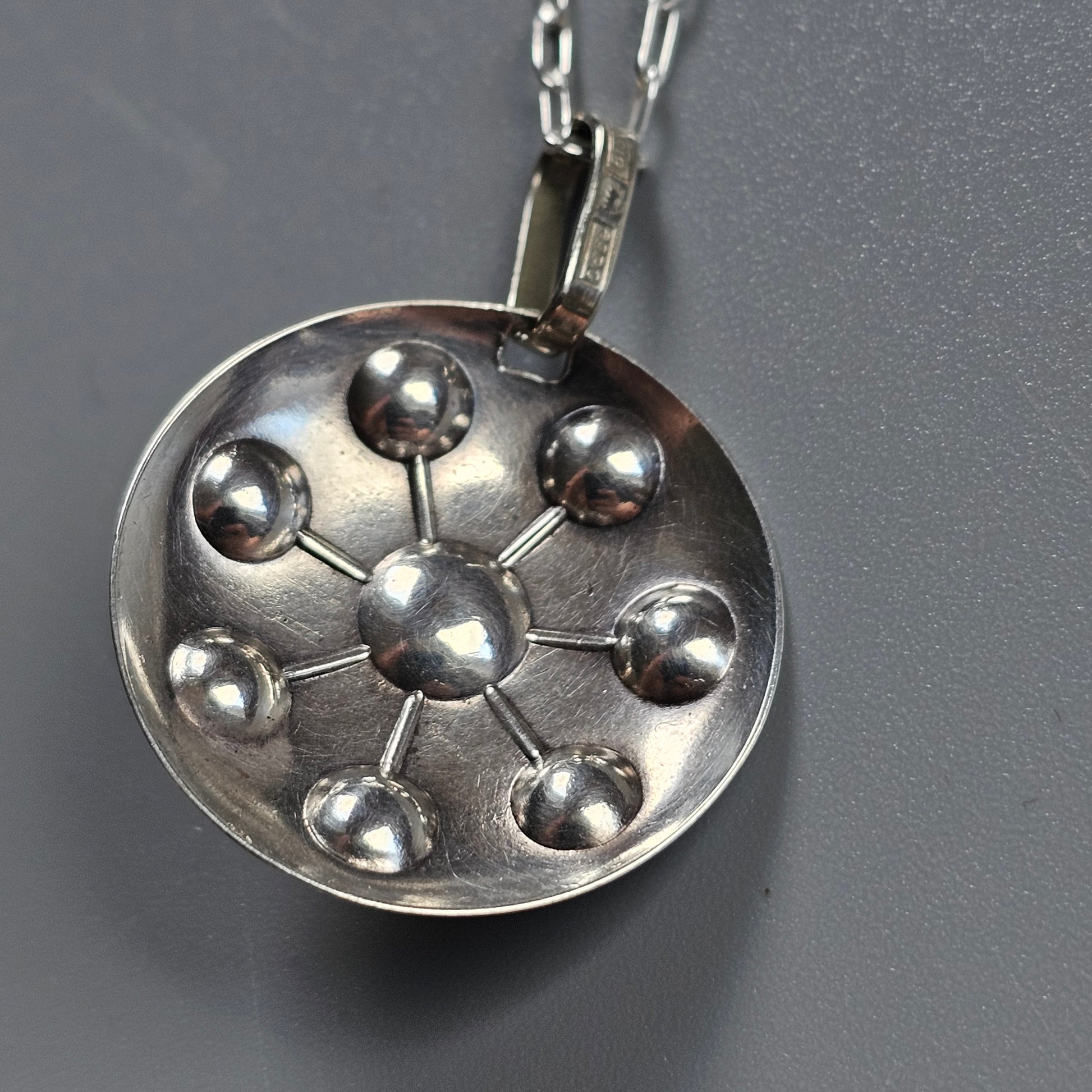 Silver pendant necklace featuring a circular design with spherical beads arranged in a radial pattern.