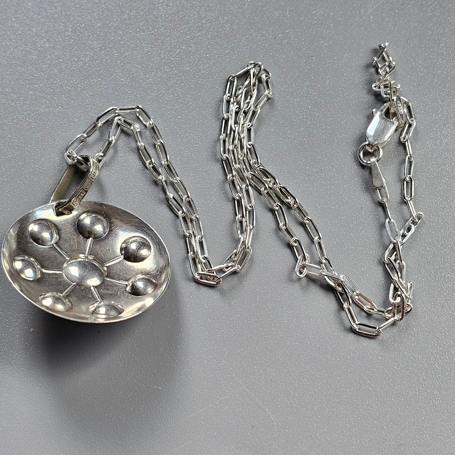 Silver pendant necklace with a circular charm featuring raised bubble-like domes.