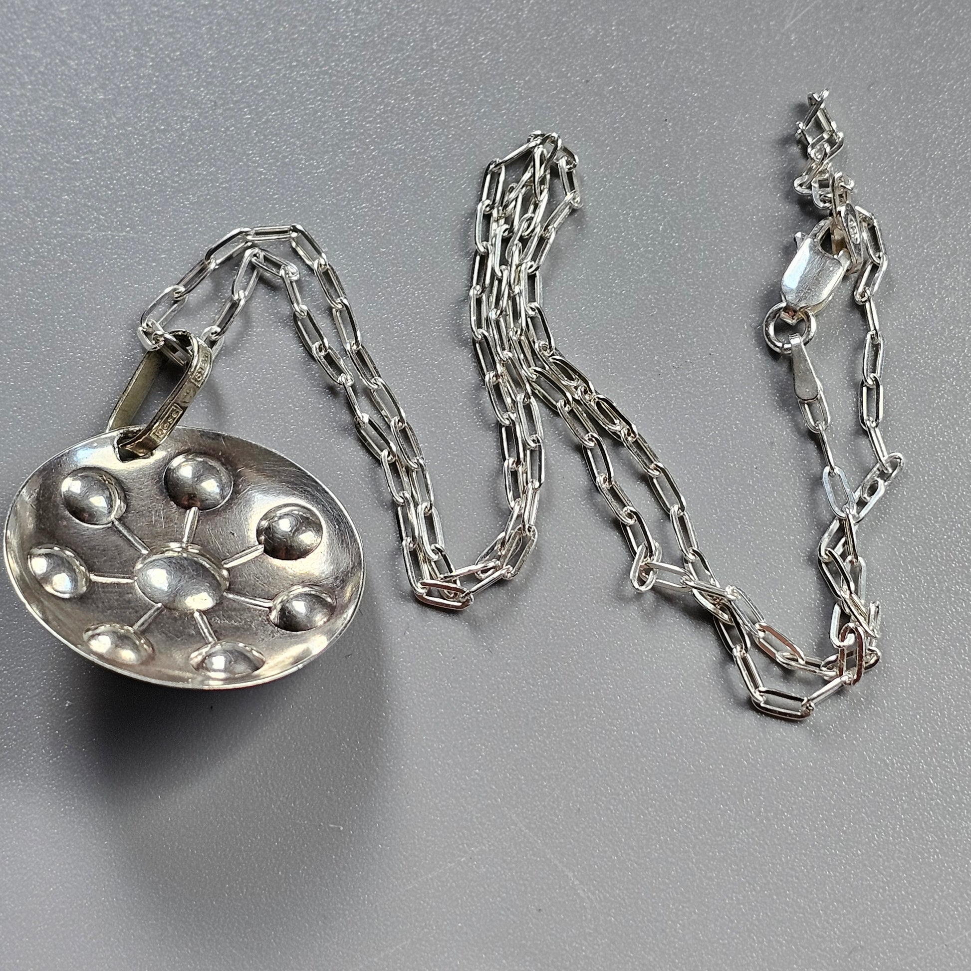 Silver pendant necklace with a circular charm featuring raised bubble-like domes.