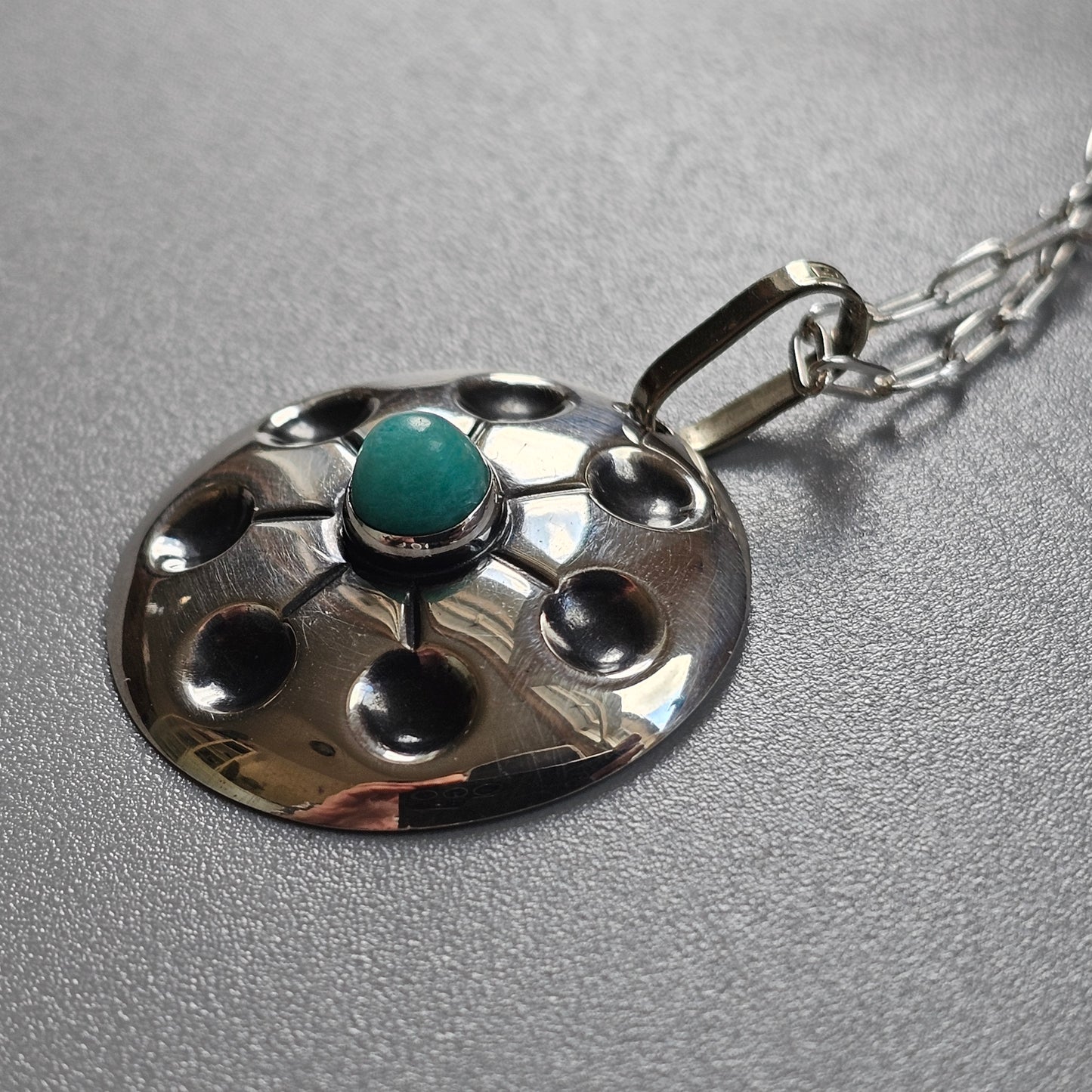 Silver pendant necklace with a circular design featuring a central turquoise stone.