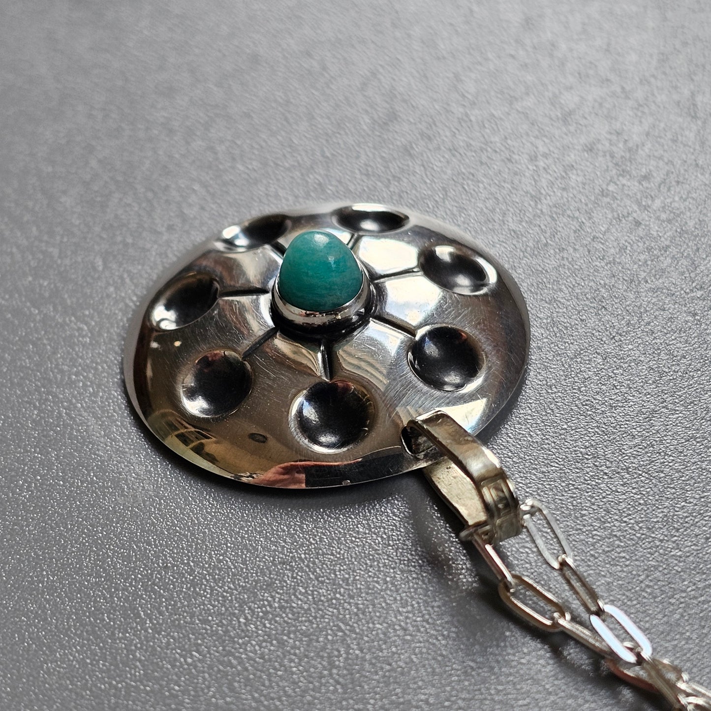 Silver pendant with a central turquoise stone surrounded by circular indentations.