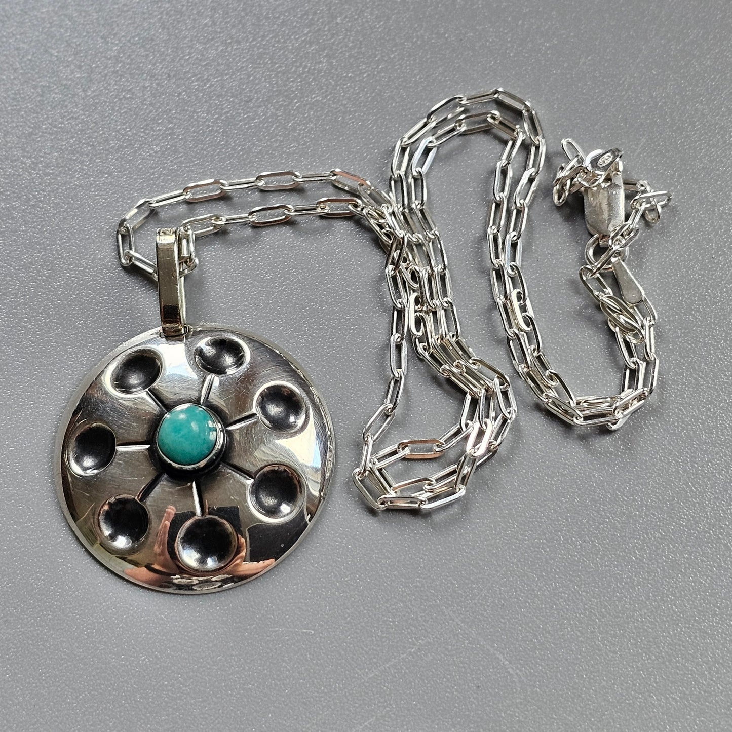 Silver pendant necklace featuring a circular design with a turquoise stone in the center.