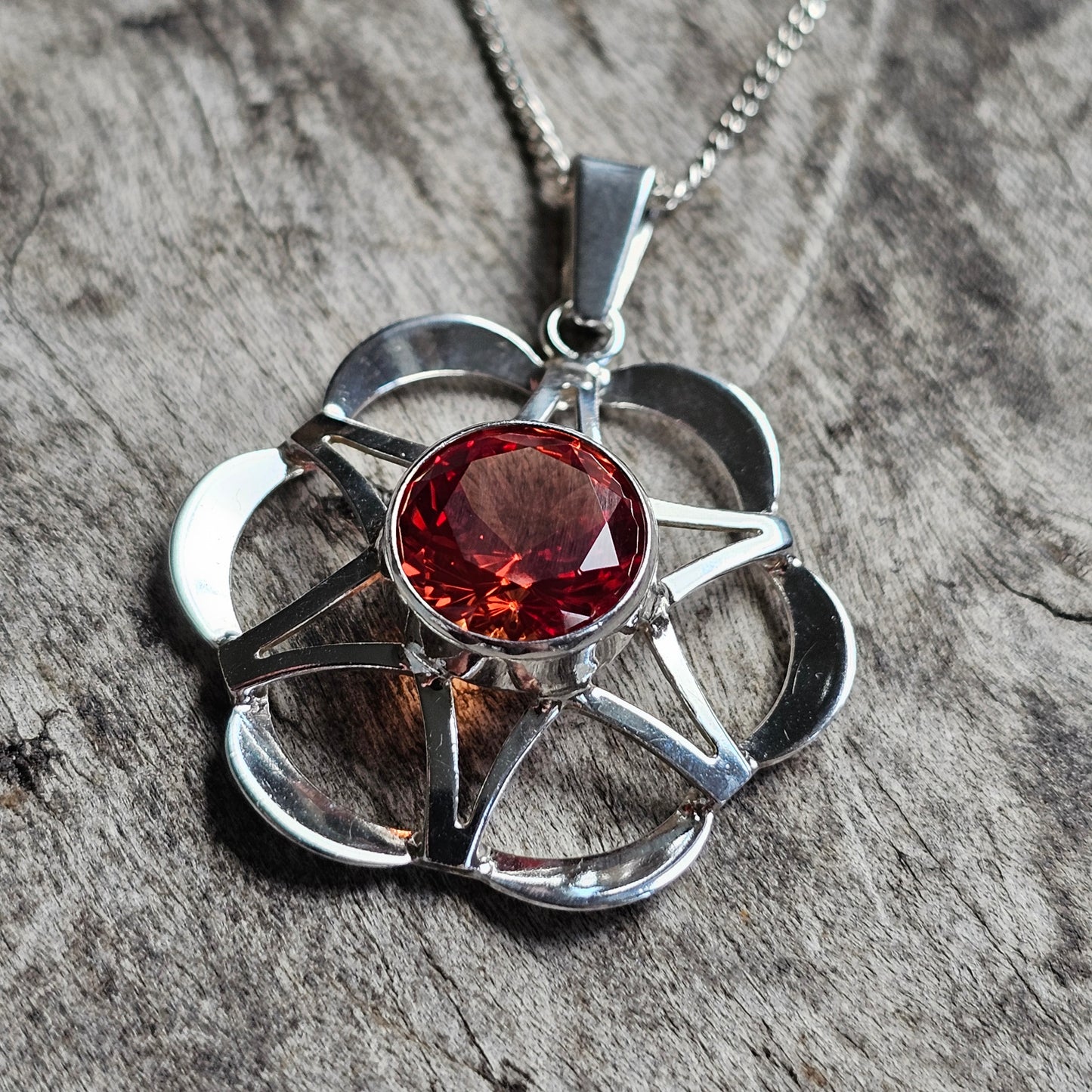 Silver pendant necklace featuring a flower-shaped design with a red gemstone center.