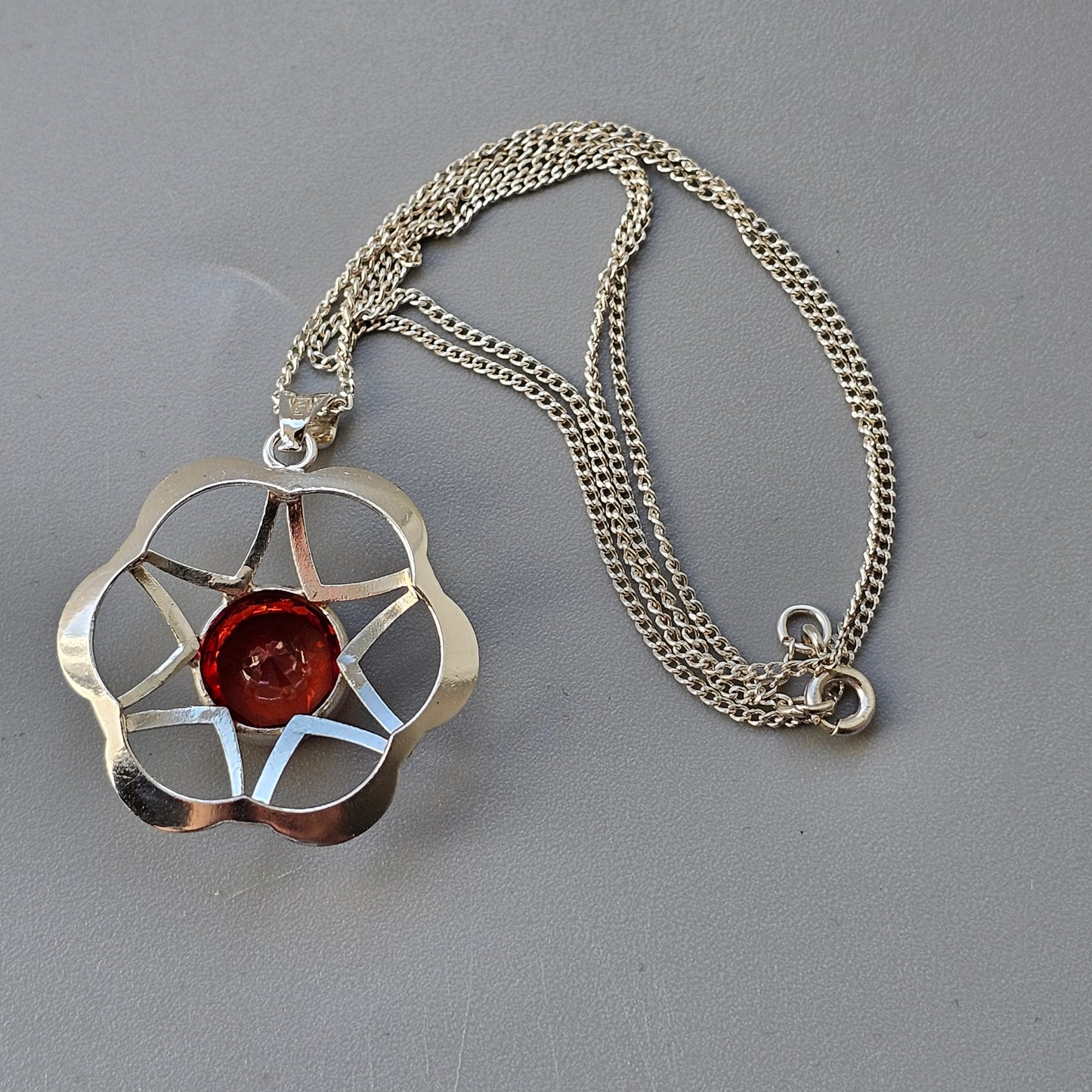 Silver pendant necklace featuring a star-shaped design with a red center stone.